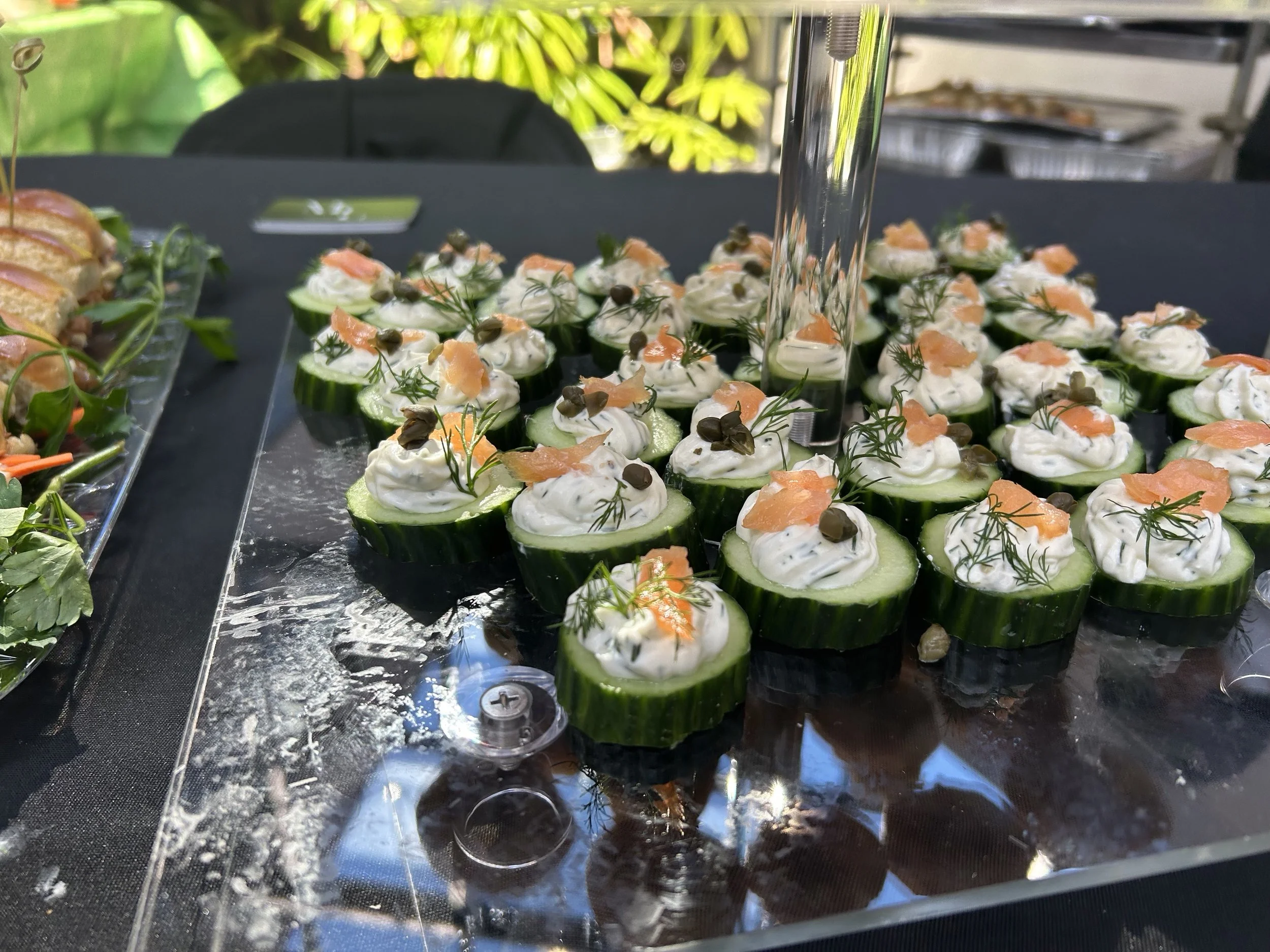 Close-up of sliced cucumber cups topped with cream cheese, smoked salmon, dill, and capers on a black surface.