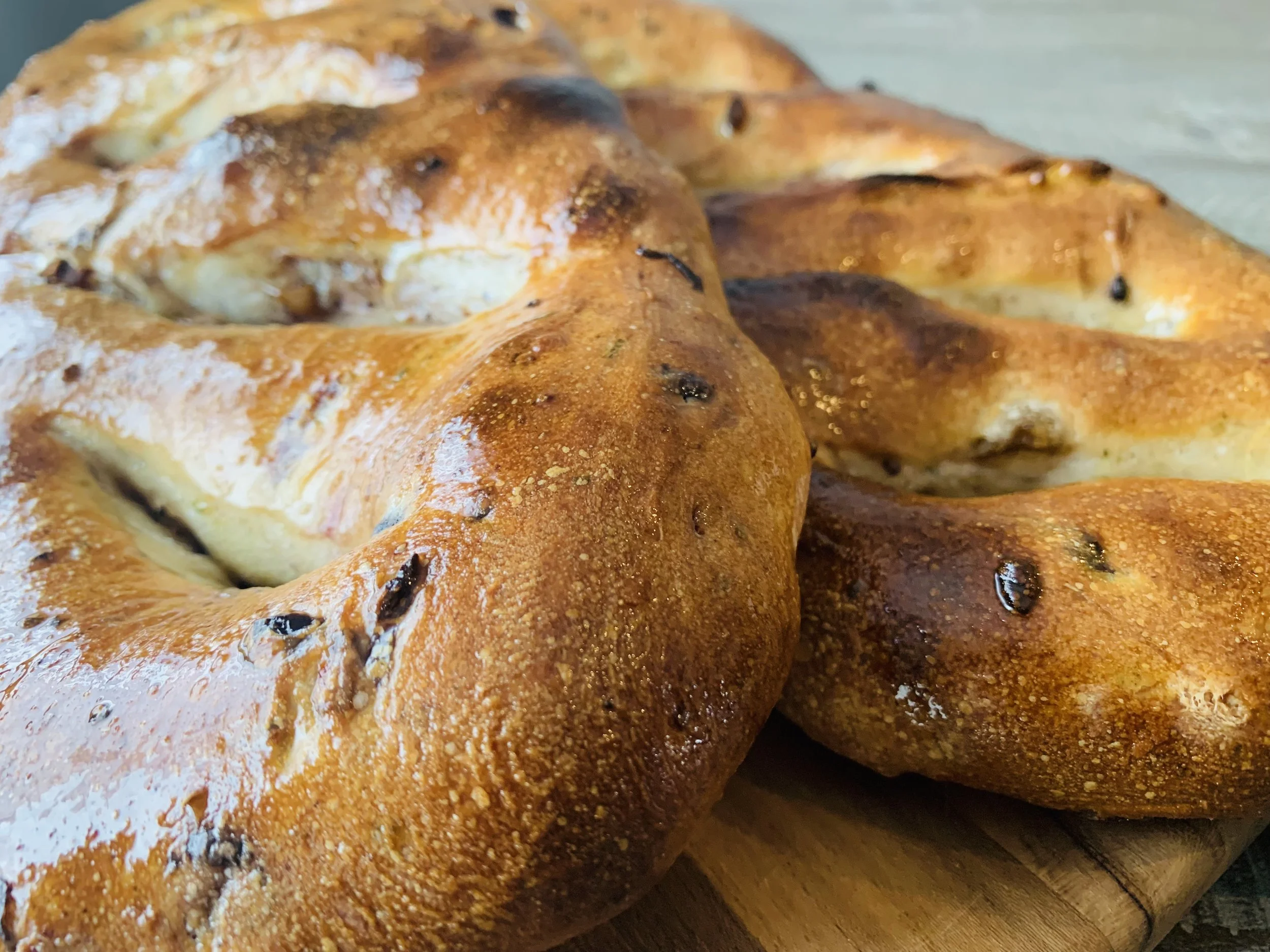 Close-up of freshly baked bagels with a golden-brown crust, some with toasted spots and visible black sesame seeds, placed on a wooden surface.