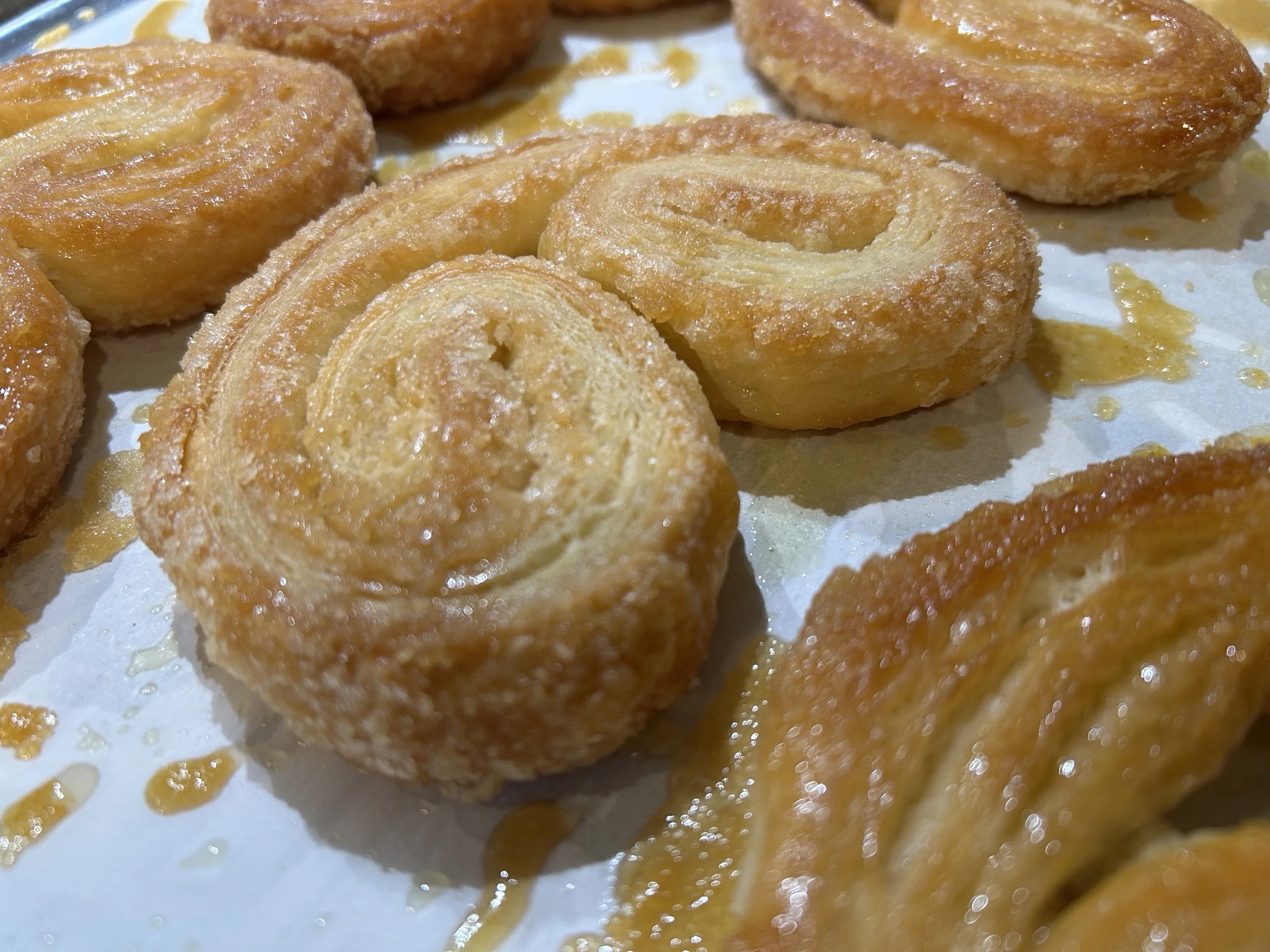 Close-up of fried churros with a golden-brown, crispy exterior, some coated with sugar and cinnamon, on a parchment paper-lined surface.