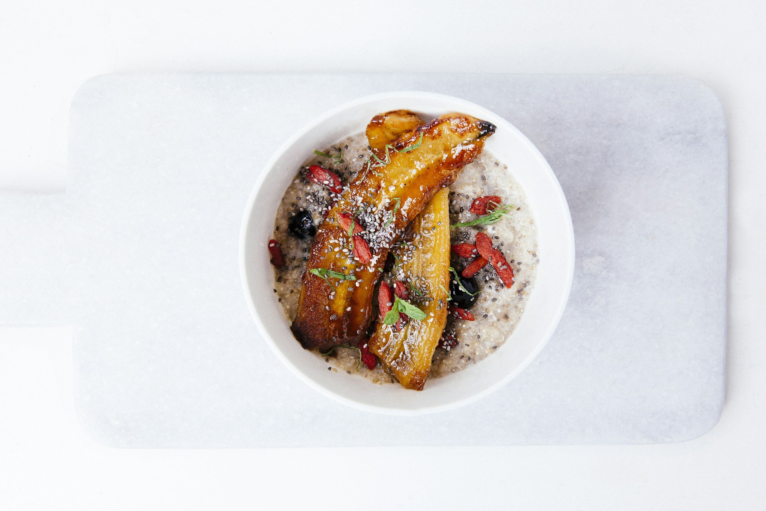 Roasted squash or sweet potato on a bowl of oatmeal garnished with goji berries, chia seeds, and herbs.
