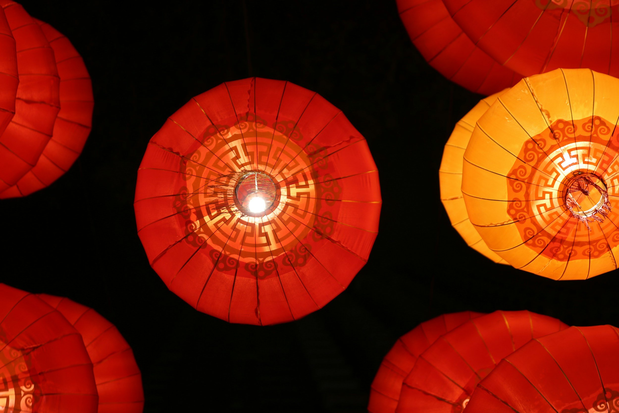 Red and yellow traditional Asian paper lanterns hanging against a dark night sky.