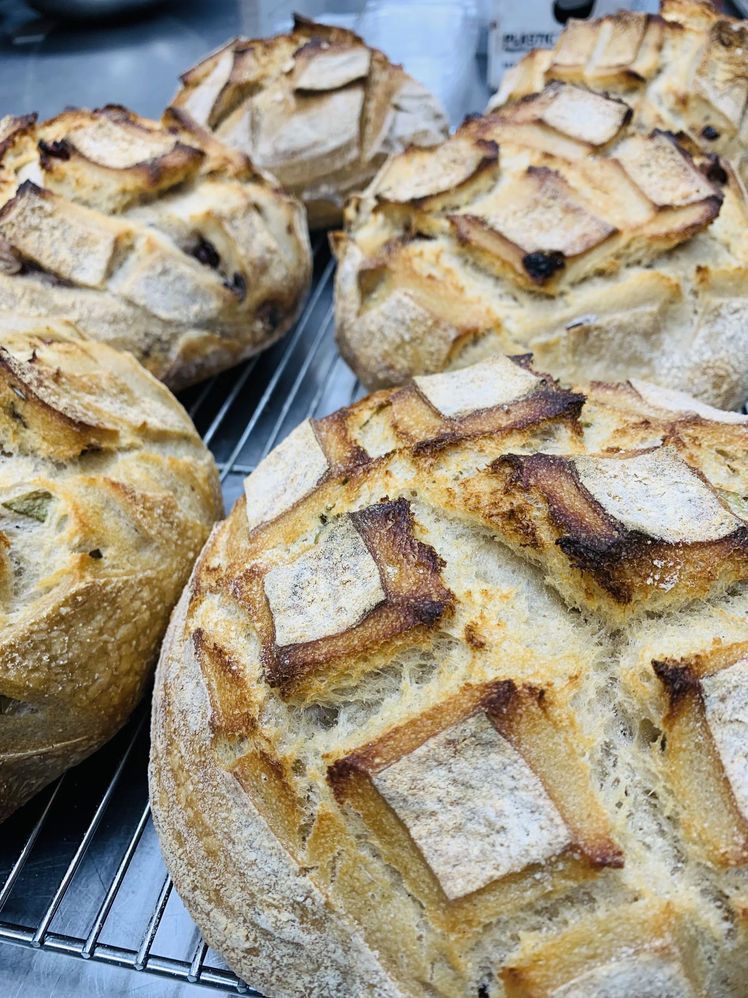Close-up of rustic loaves of bread with a golden crust and scoring, cooling on a wire rack.