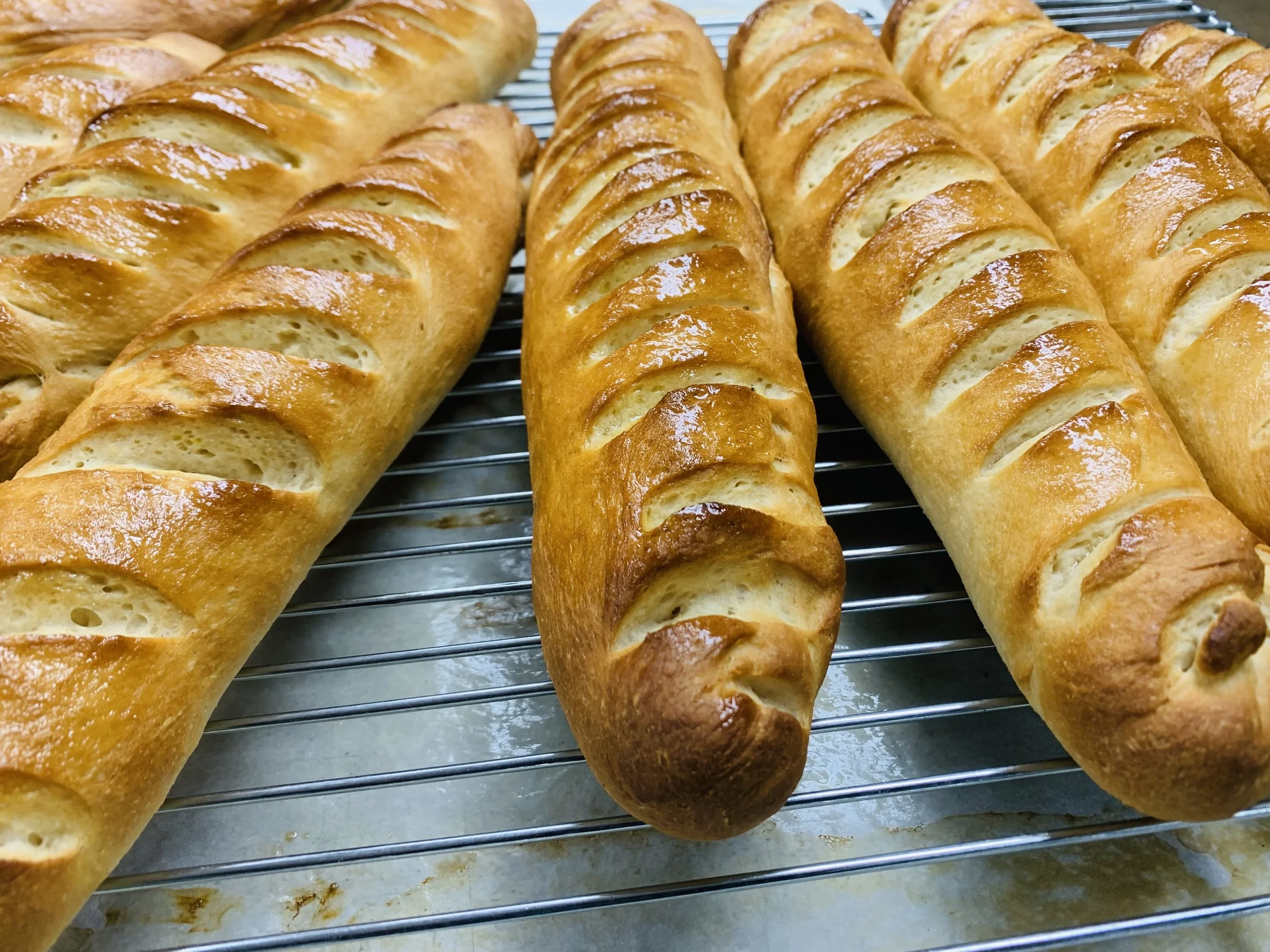 Golden-brown baguettes cooling on a wire rack, with diagonal slashes on top.