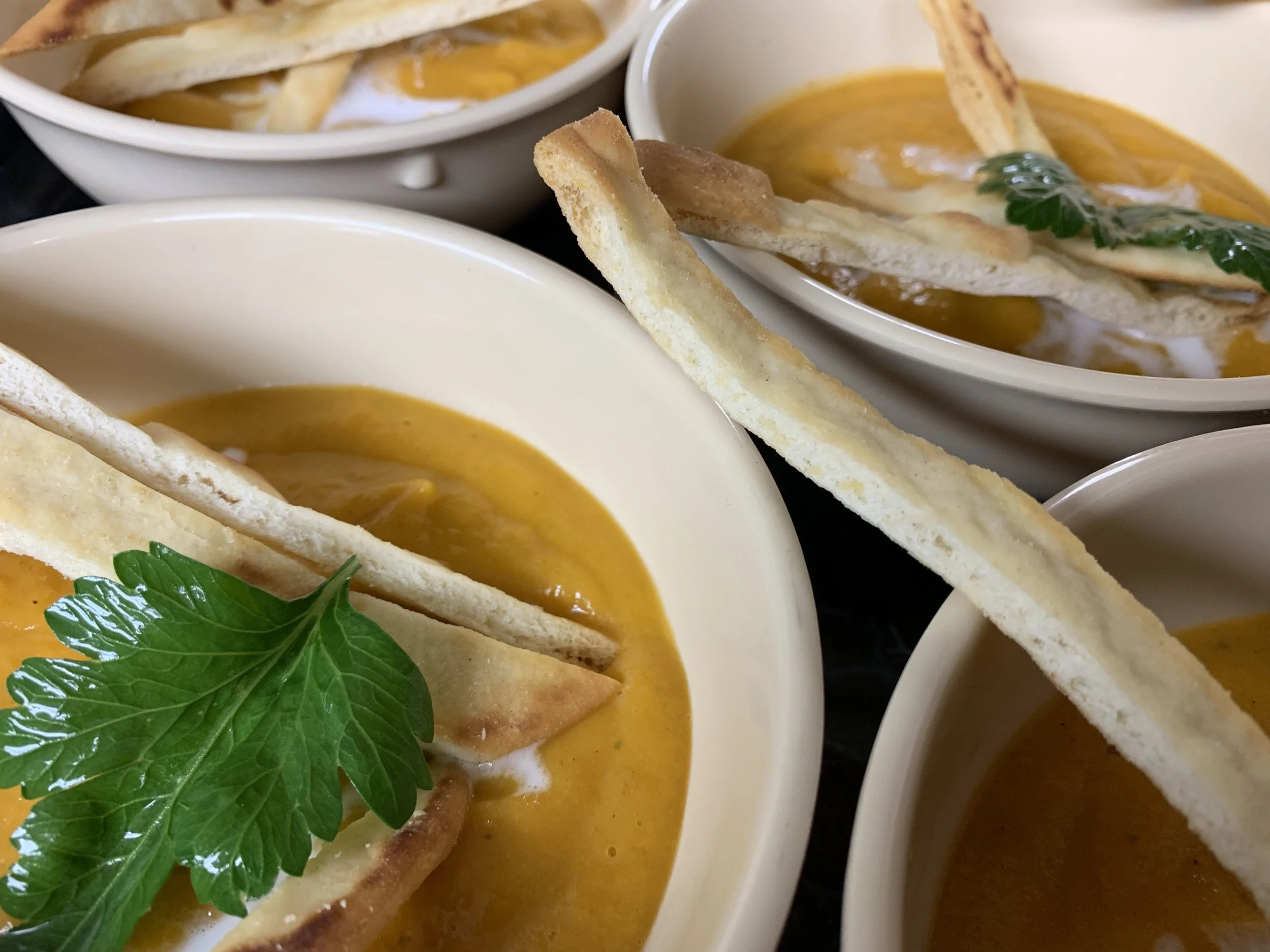 Close-up of bowls of creamy pumpkin soup garnished with fresh basil and served with crispy bread slices.