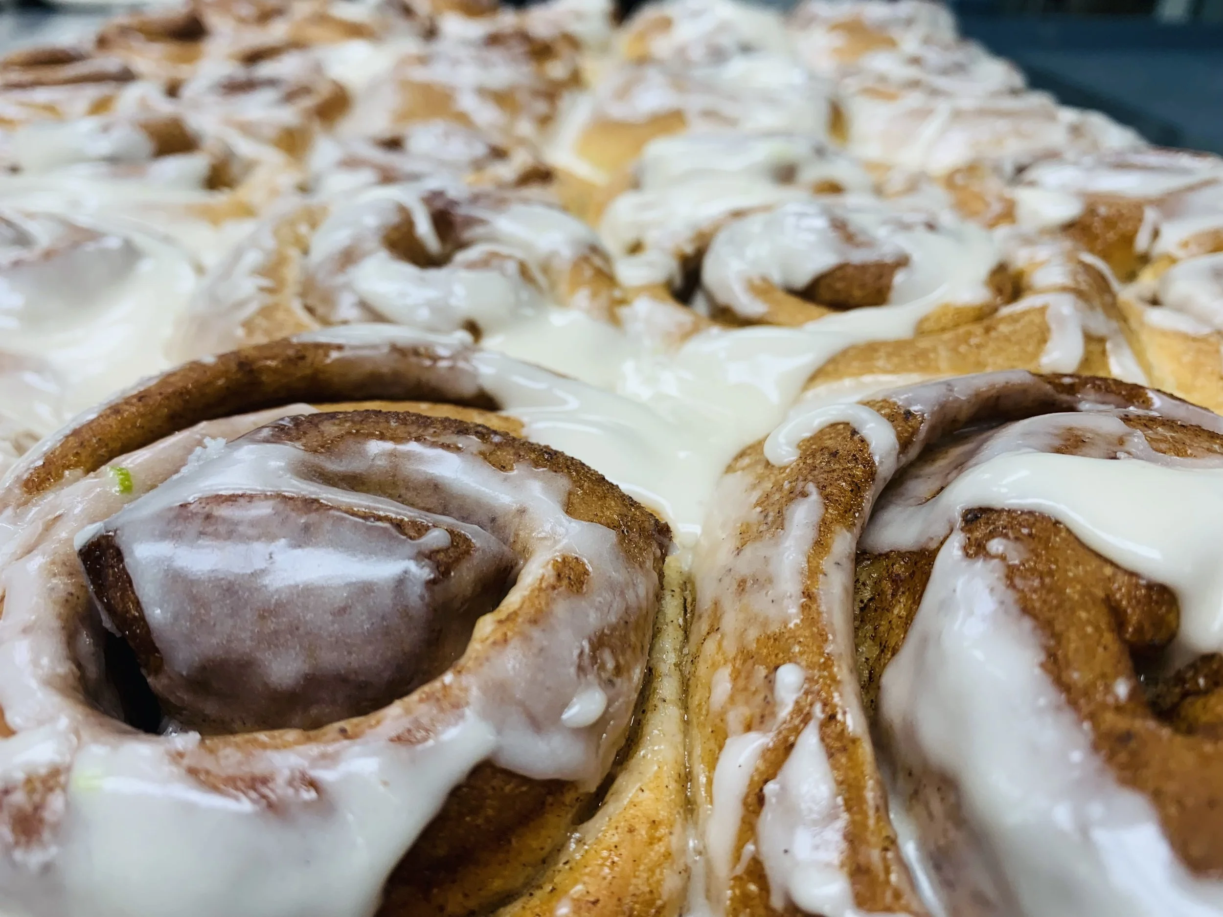 Close-up of several cinnamon rolls topped with white icing, with a fluffy and golden-brown appearance.