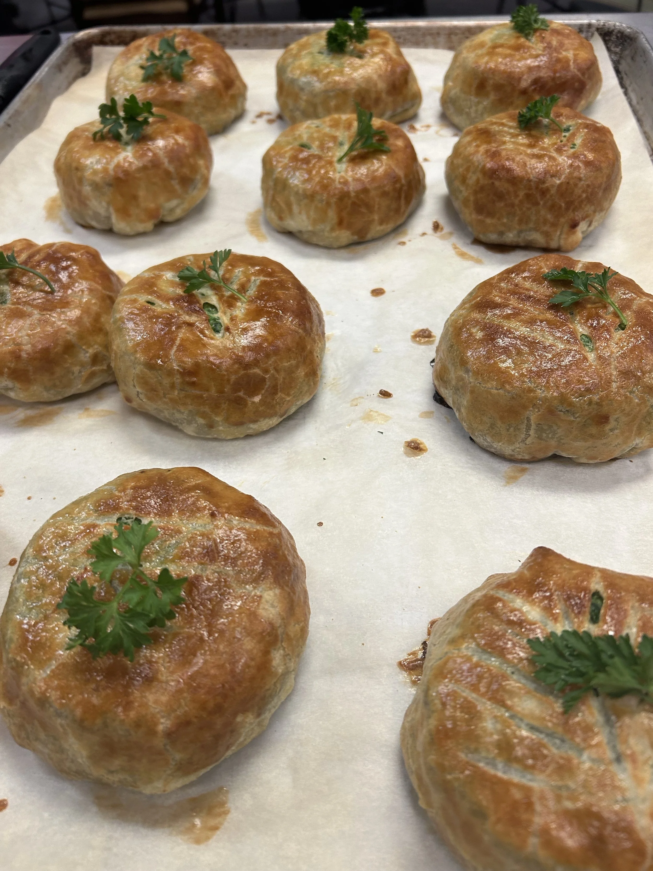 Baked meatballs topped with fresh parsley on a baking sheet covered with parchment paper.