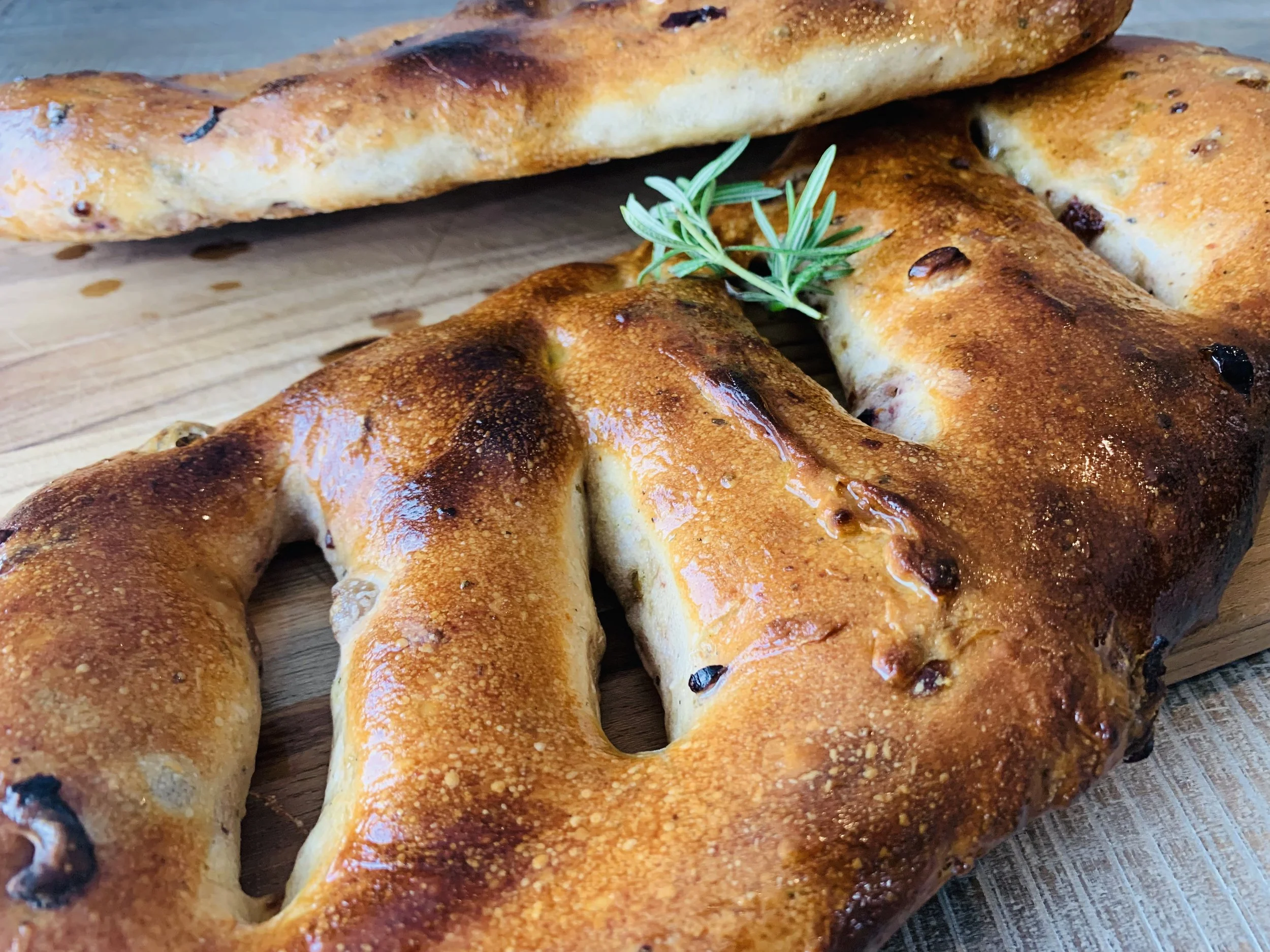 Close-up of freshly baked, golden brown bagels on a wooden board, garnished with a sprig of rosemary.