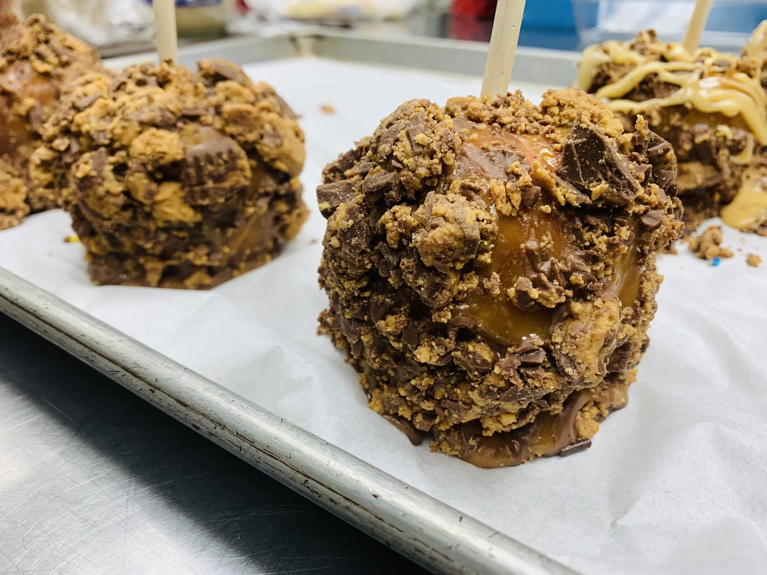 Chocolate-covered caramel cake pops with crushed cookie toppings on a baking sheet.
