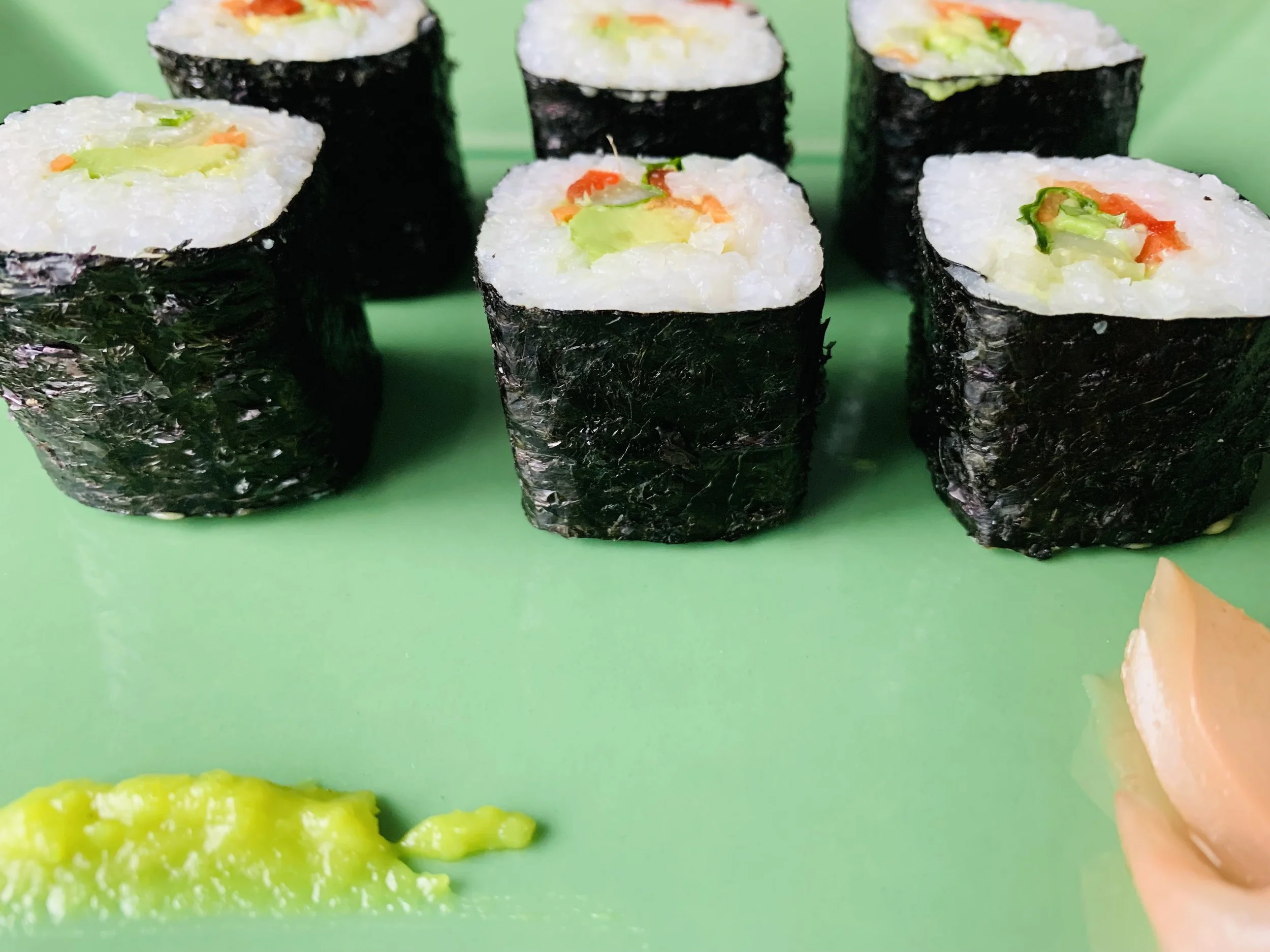 Close-up of five Japanese sushi rolls on a green surface, each wrapped in black seaweed with white rice and various colorful vegetables inside.