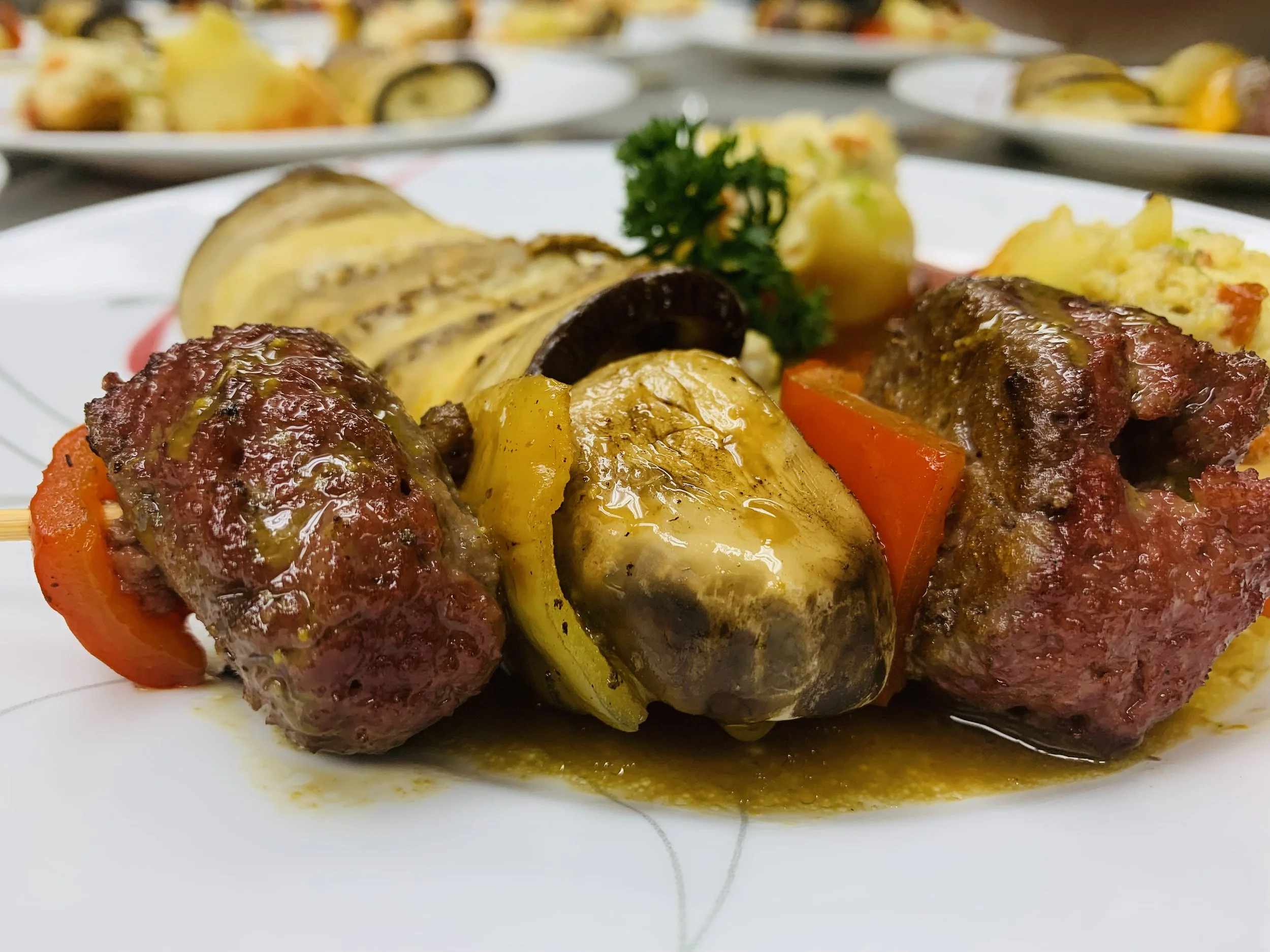 Close-up of meat and vegetable skewer with peppers, zucchini, and a sprig of parsley on a white plate