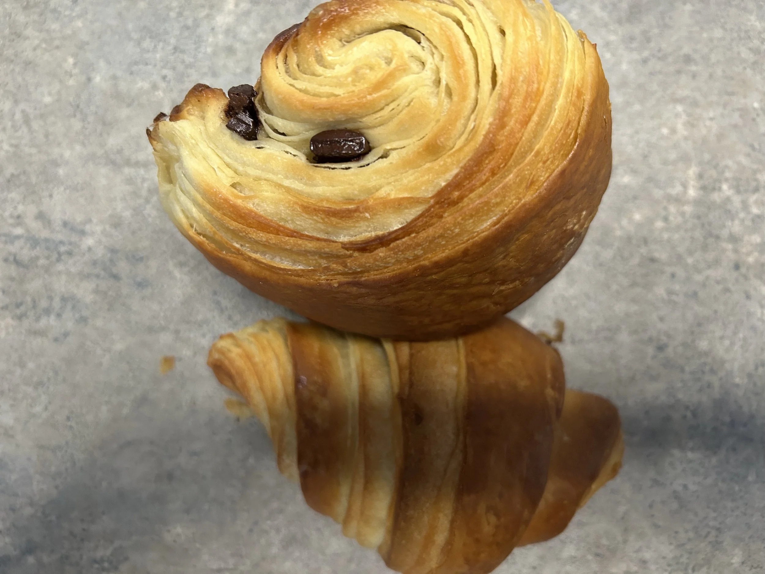 A close-up of a rolled pastry with chocolate chips on top, resting on a gray surface.
