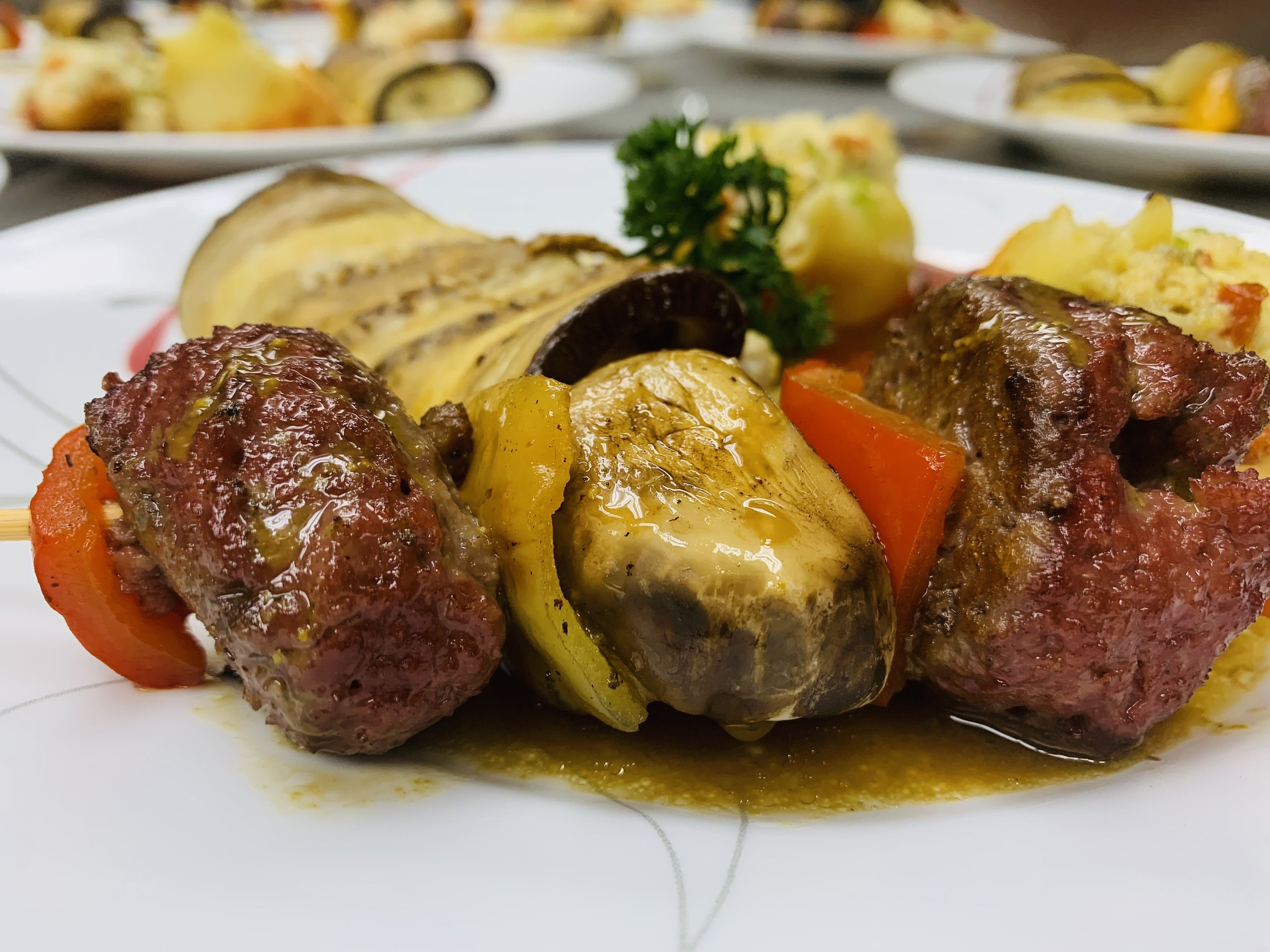 Close-up of grilled meat skewers with grilled vegetables and a sprig of parsley on a white plate.