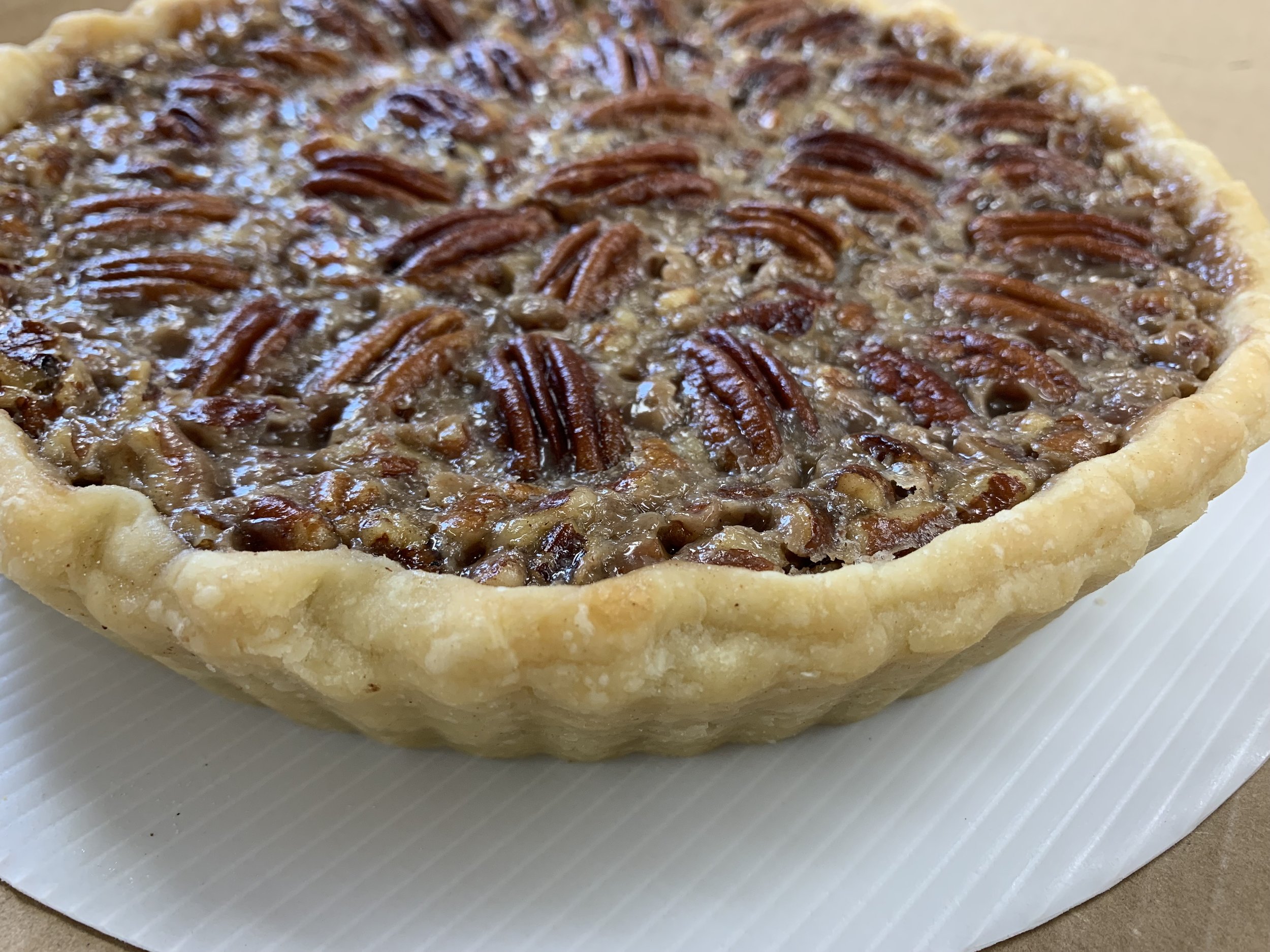 Close-up of a pecan pie, showing a flaky crust filled with caramelized pecans and syrup, on a white surface.
