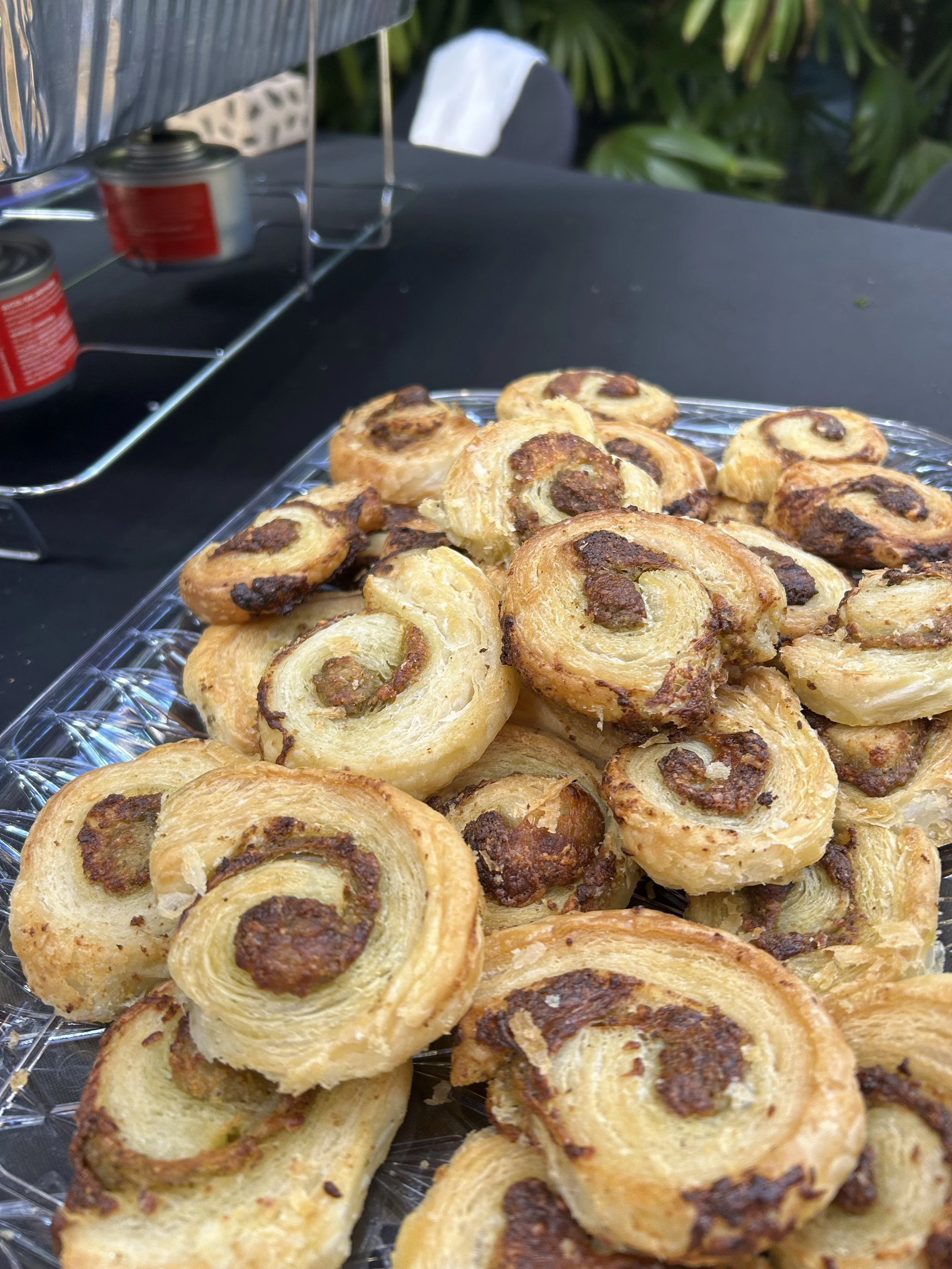 Close-up view of a tray of freshly baked cinnamon rolls with chocolate chips on top, arranged on a clear glass platter.