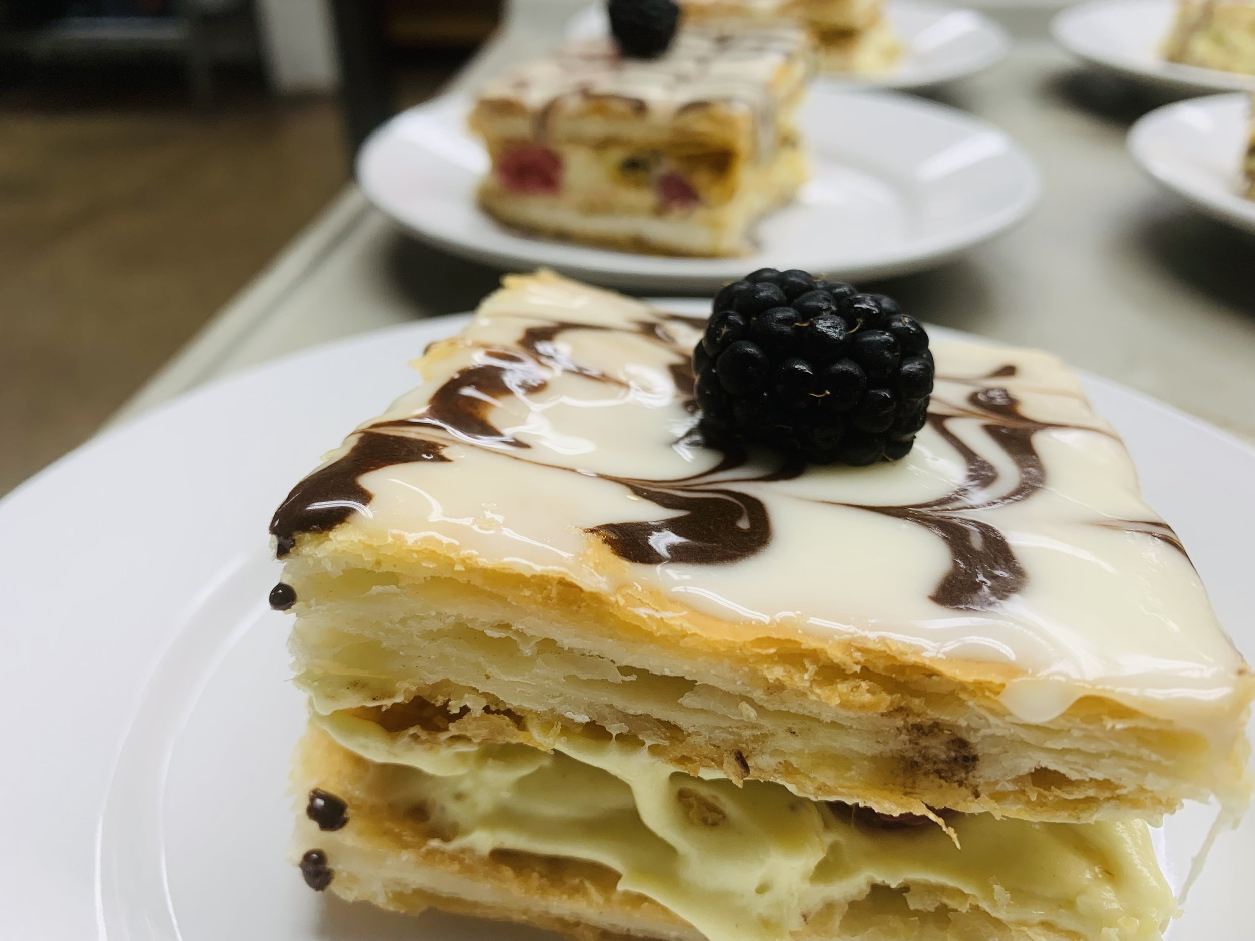 A slice of layered cake topped with a blackberry and drizzled with white and dark chocolate sauces on a white plate.