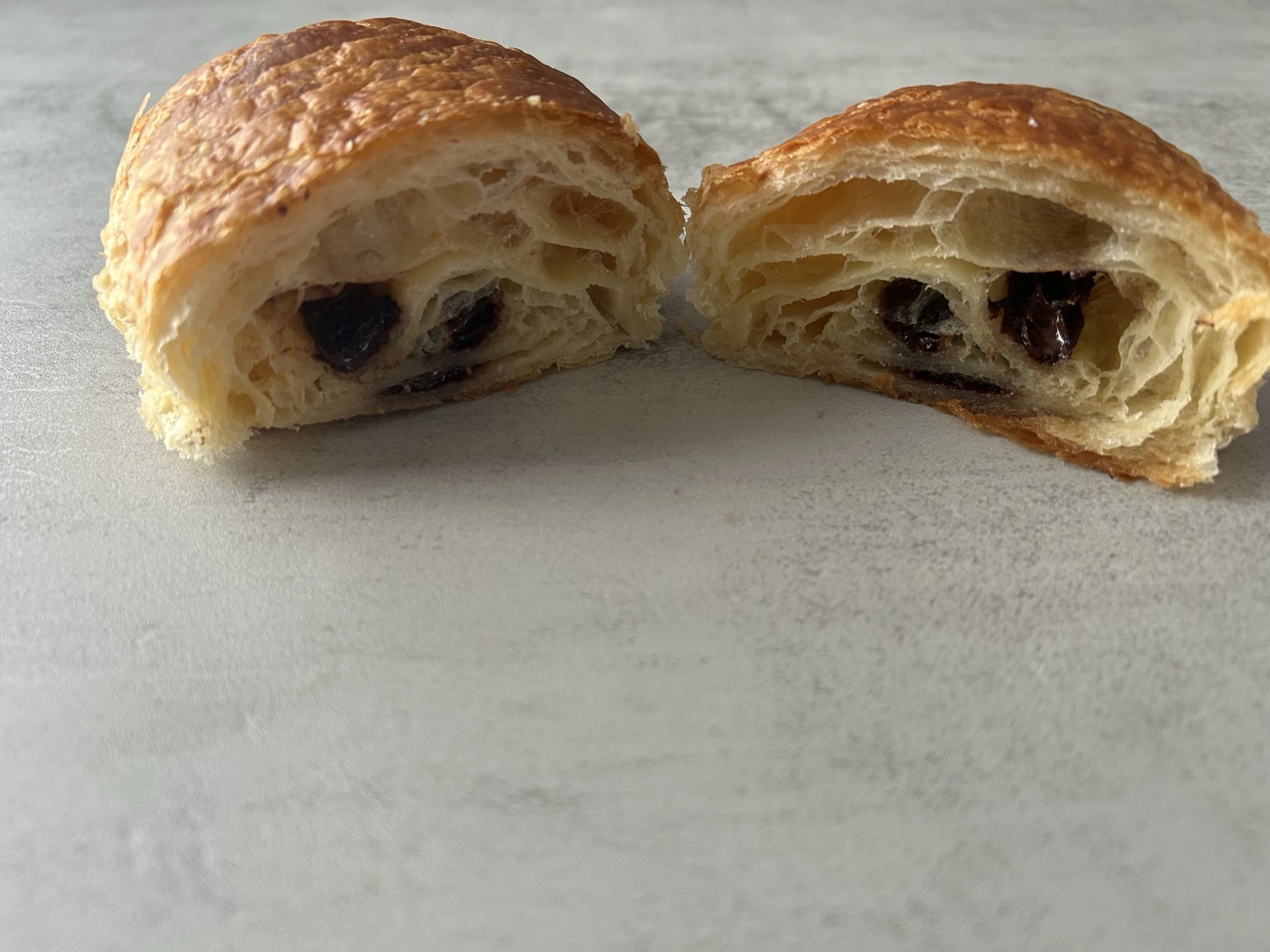 A close-up of a croissant pastry that has been broken in half, revealing its flaky, layered interior filled with dark chocolate chips.