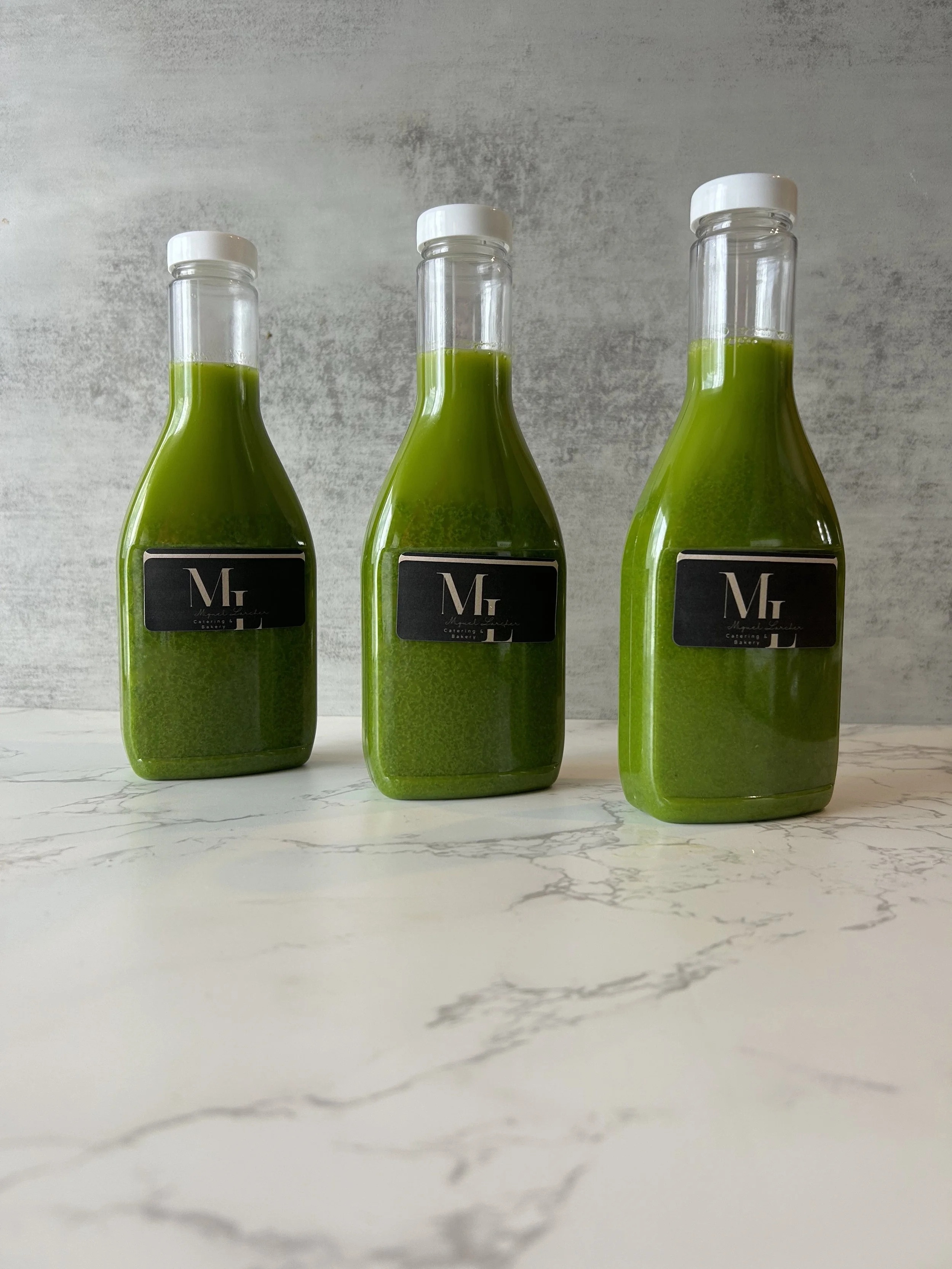 Three bottles filled with green liquid placed on a white marble surface with grey background.