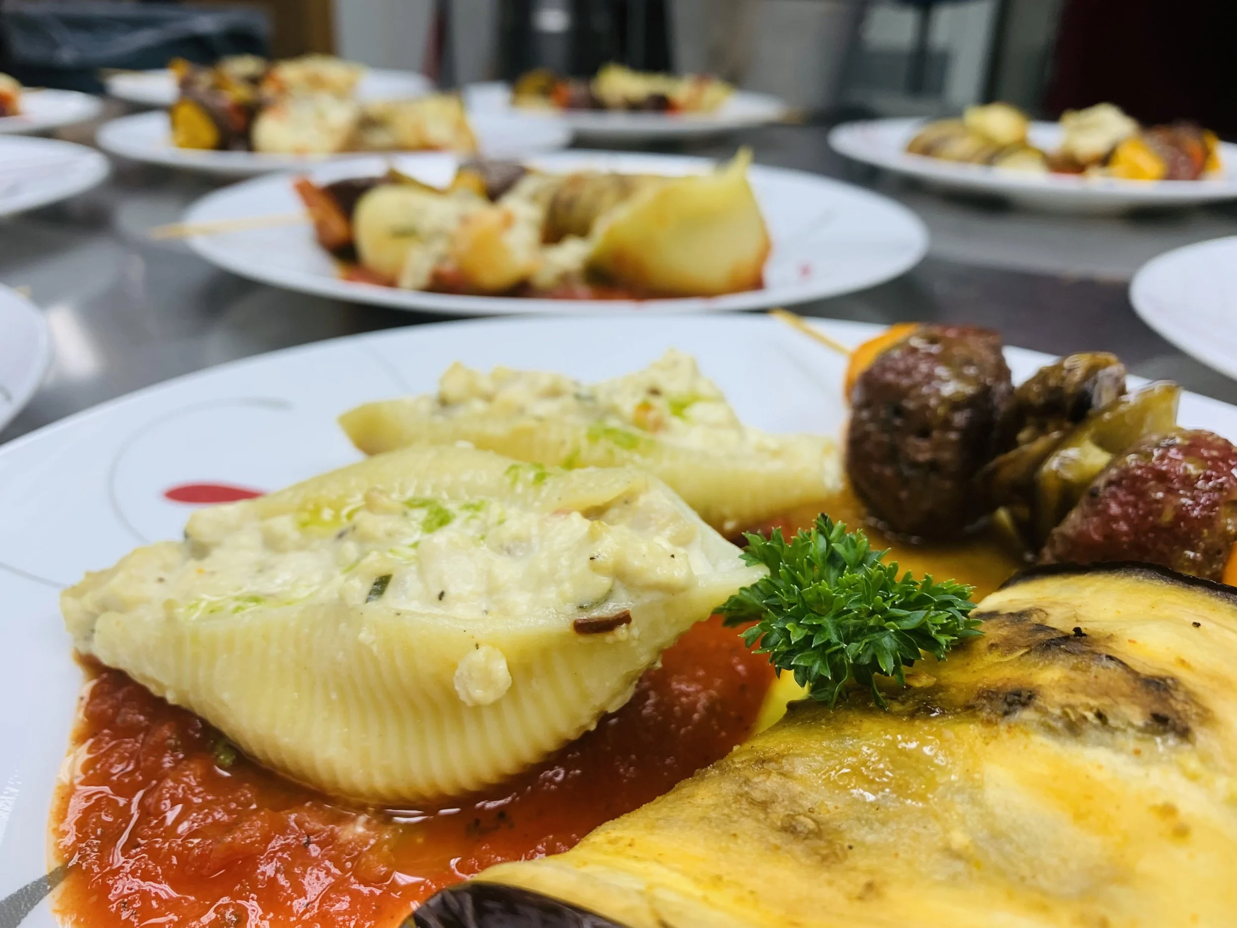 A plate of baked lasagna topped with cheese, surrounded by meatballs, roasted vegetables, and garnished with parsley.