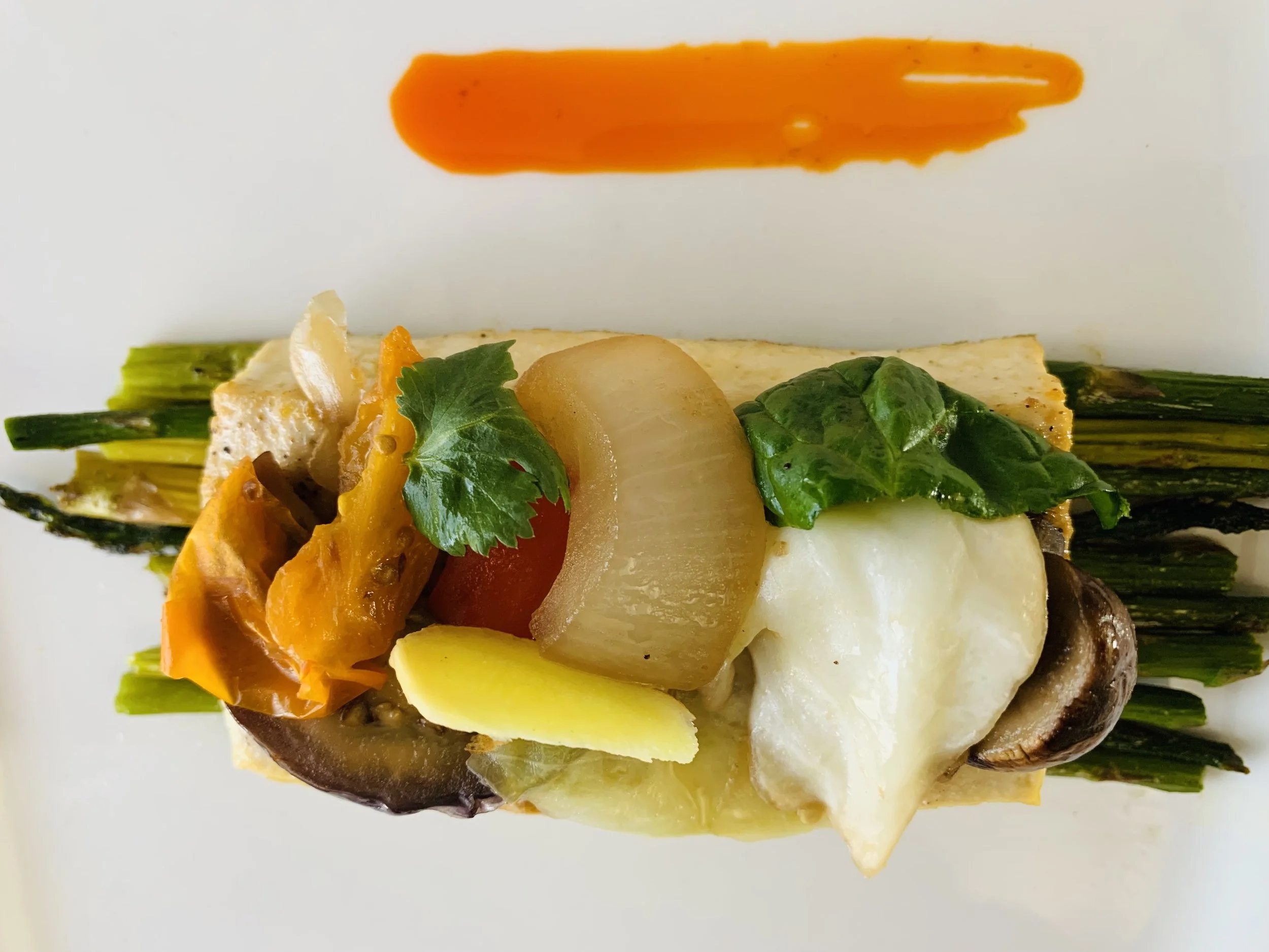 Close-up of a gourmet dish with grilled vegetables, cheese, and herbs on a white background.