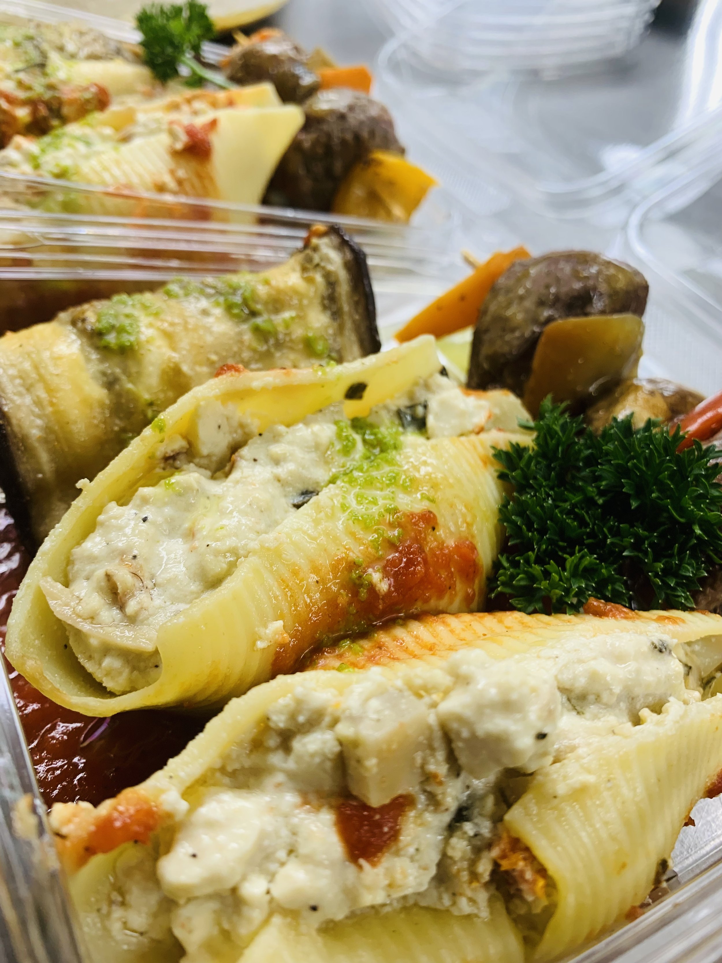 Close-up of pasta and vegetable lasagna with layers of pasta, cheese, vegetables, and sauce in a clear plastic container.