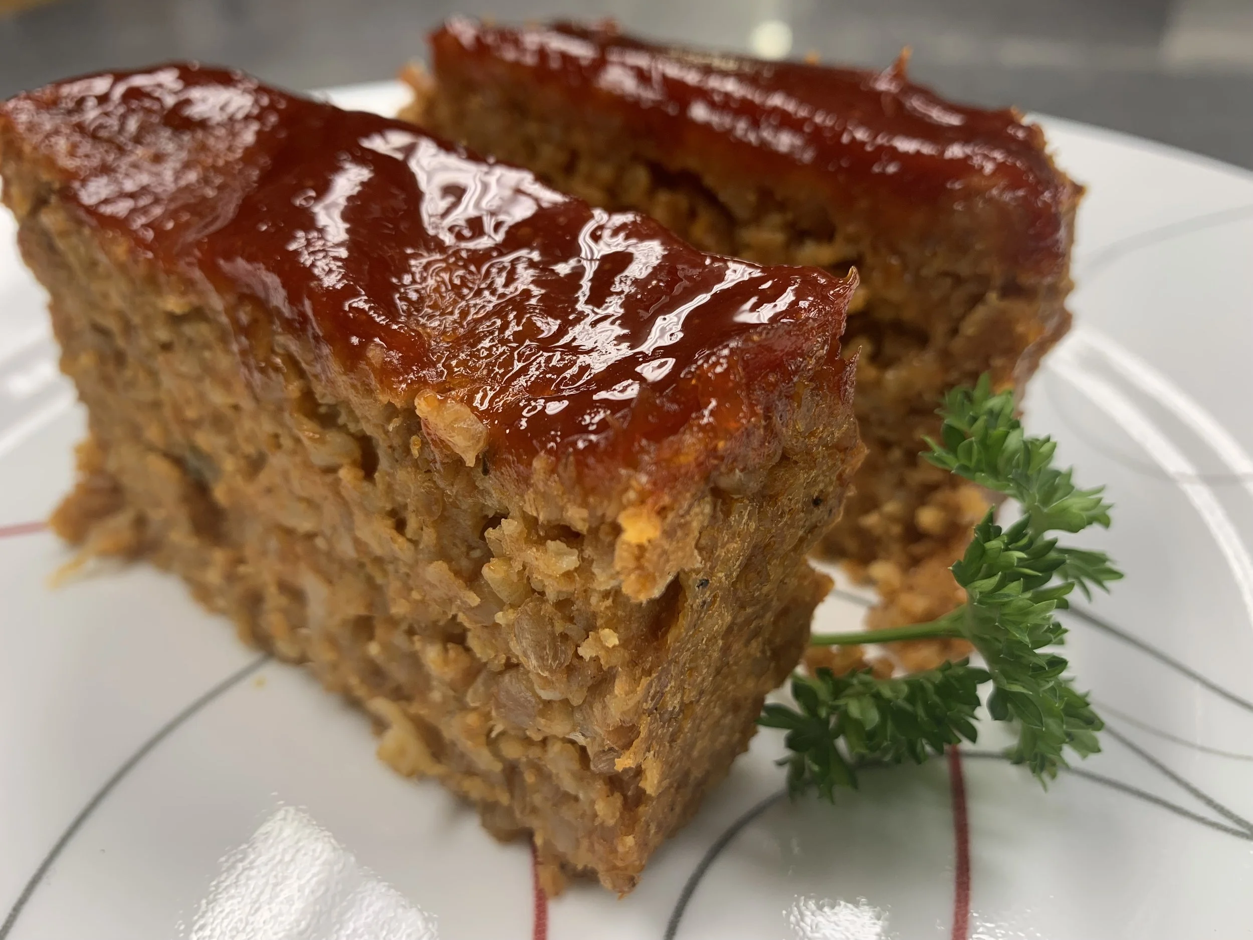 Two slices of meatloaf glazed with ketchup on a white plate garnished with parsley
