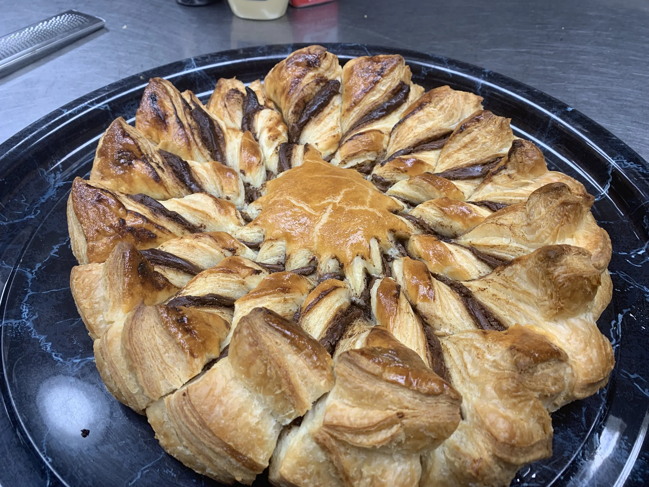 Close-up image of a plate of sliced, freshly baked puff pastry with chocolate filling, arranged in a circular pattern on a black serving tray.