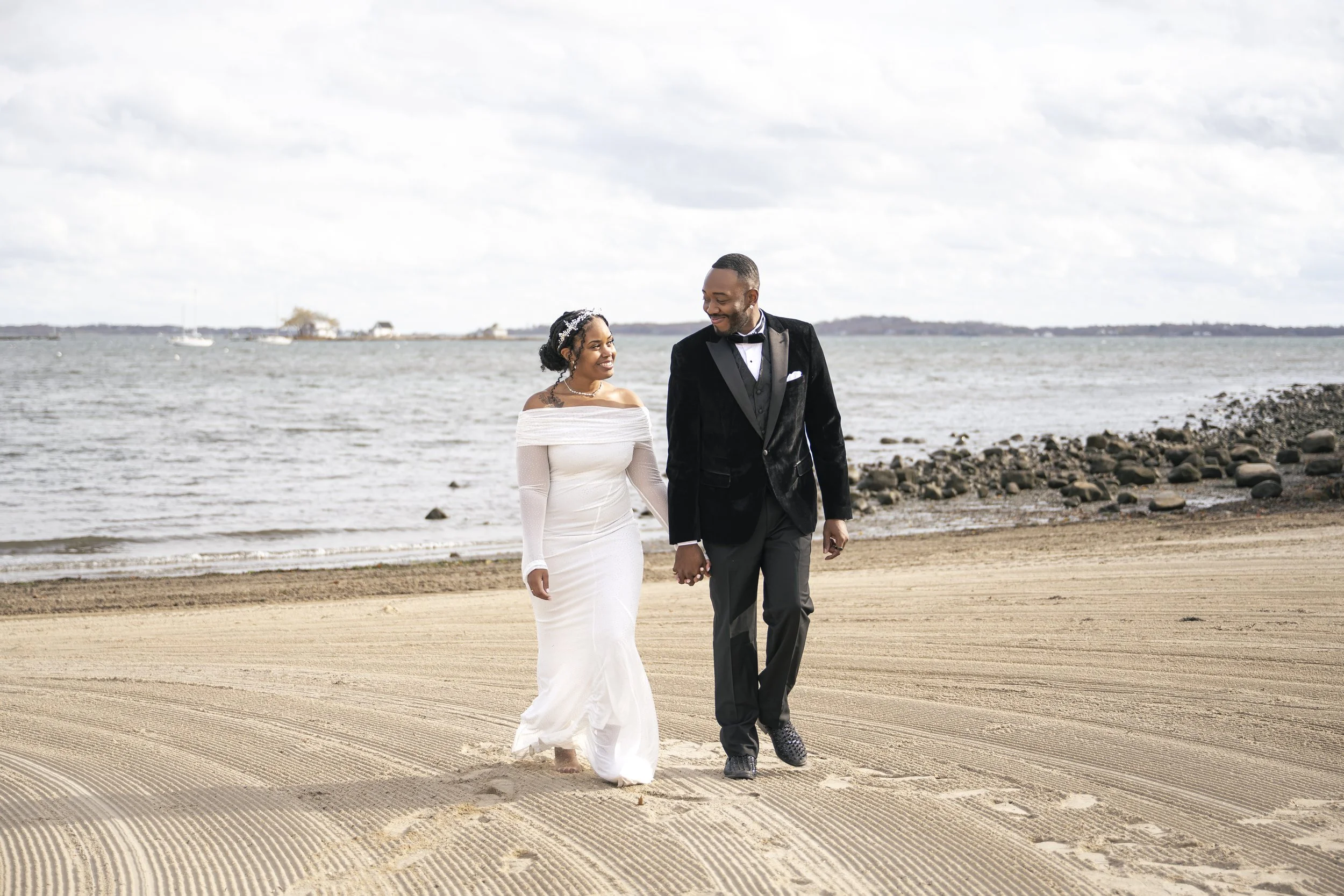 A bride and groom standing outdoors with forest and lake in the background, holding foreheads and gazing into each other's eyes on their wedding day.
