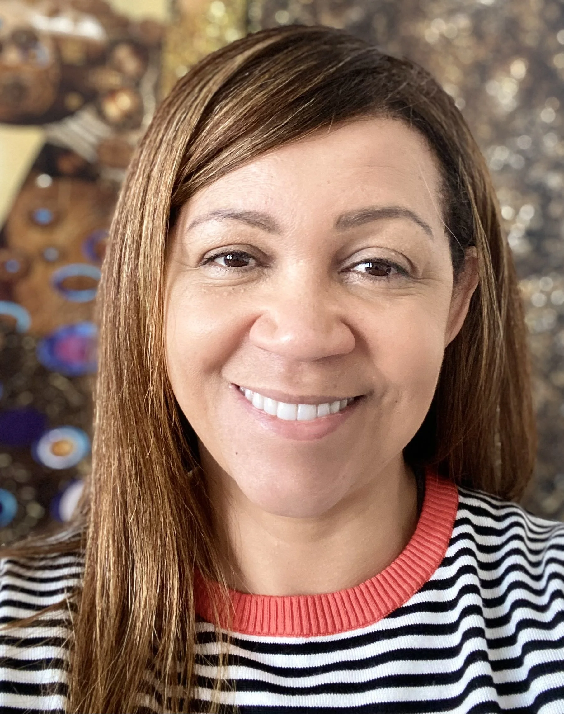 Woman smiling with long hair and striped shirt, blurred decorative background.