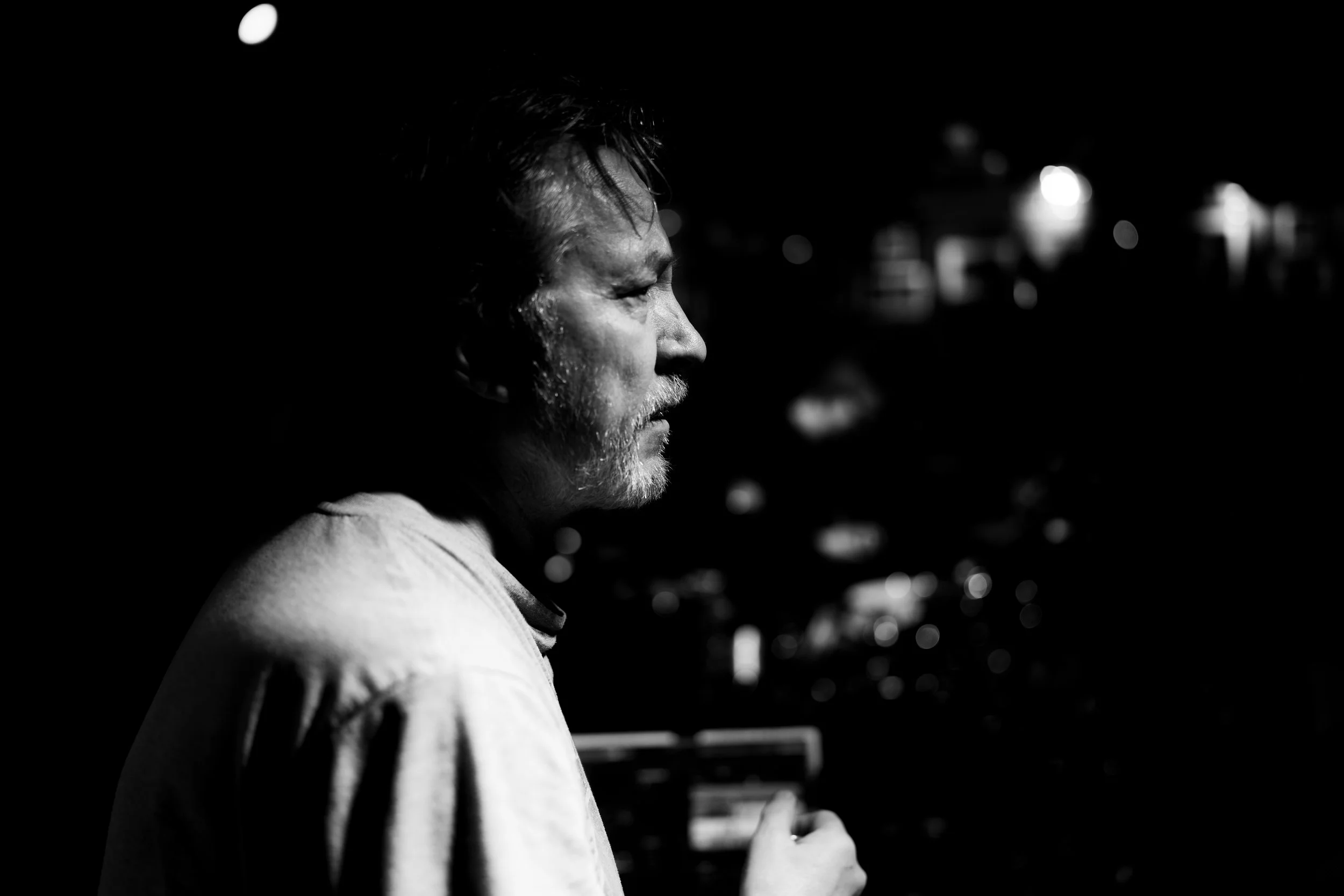 A black and white photo of Nils Petter Molvaer illuminated by light, with a dark background.