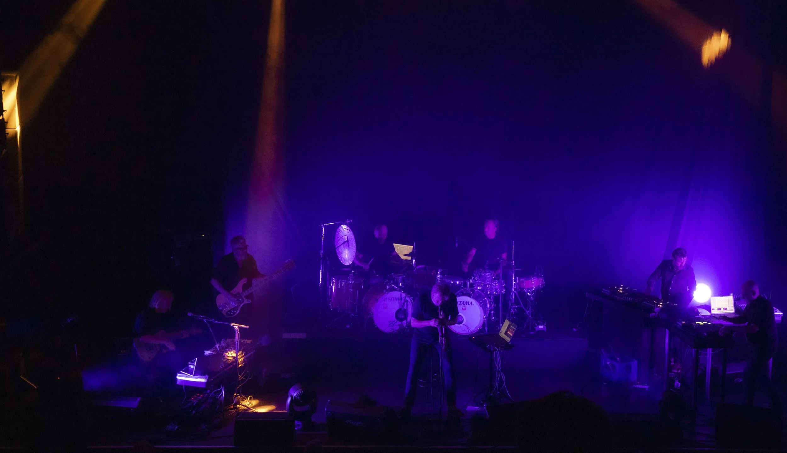 Nils Petter Molvaer 's Khmer on stage with purple and orange stage lighting, including a drummer, a keyboard player, and a guitarist.