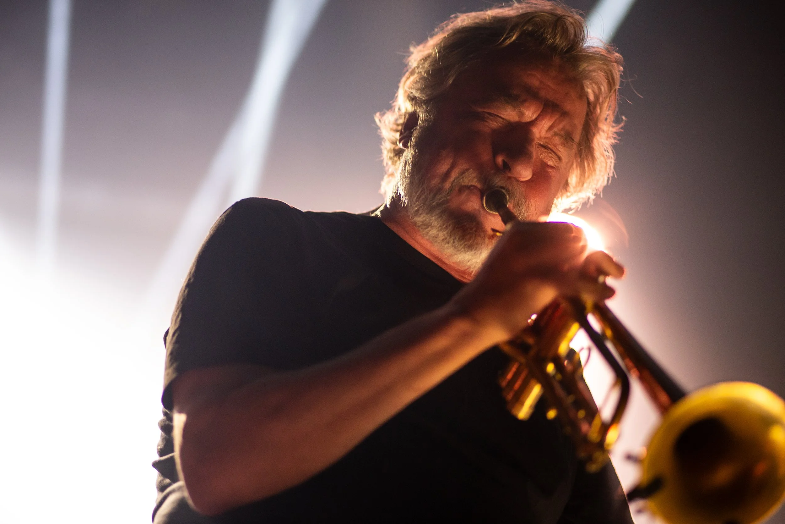 An elderly man playing a trumpet on stage with dramatic lighting.