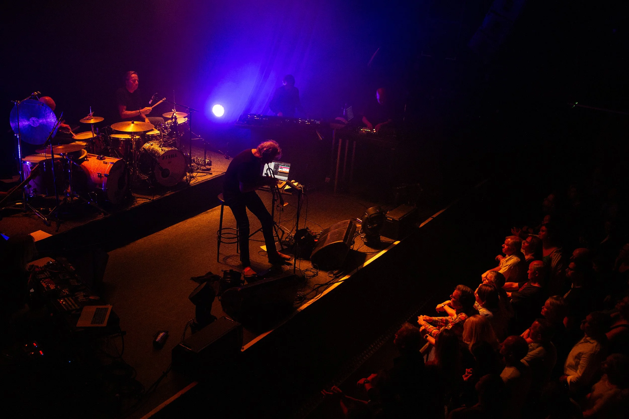 Musicians performing on stage with an audience watching in a dark concert hall