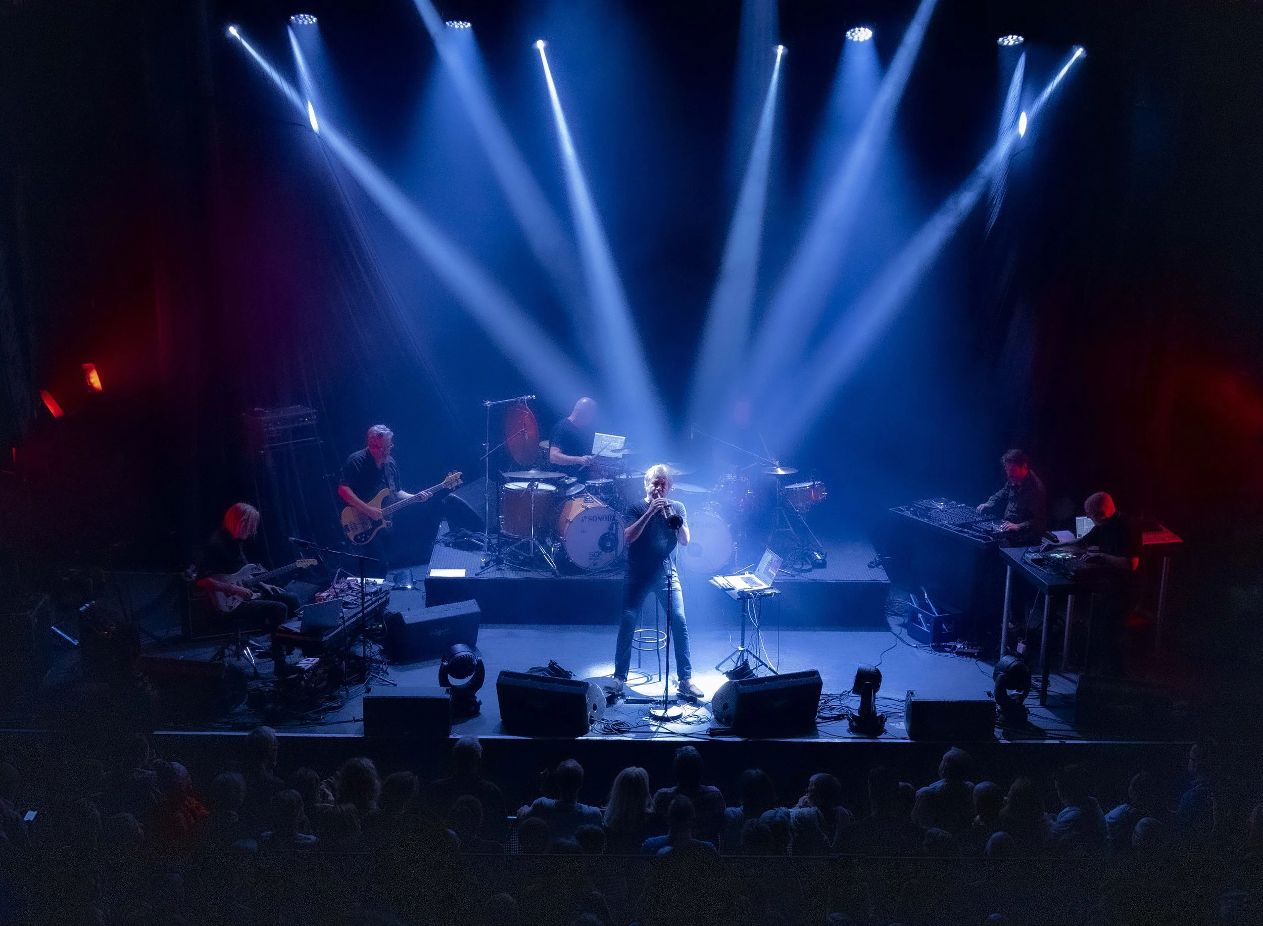 Nils Petter Molvaer 's Khmer performing on stage with blue spotlights and audience watching.