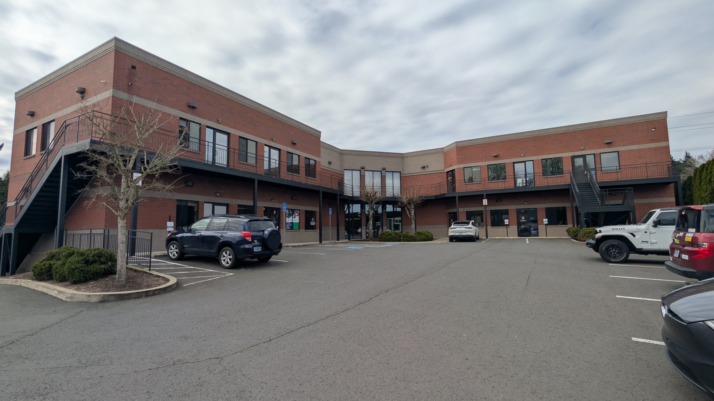 Exterior view of the professional office building for Wise Touch Bodywork in Tigard, showing the two-story brick and grey siding entrance and parking lot.