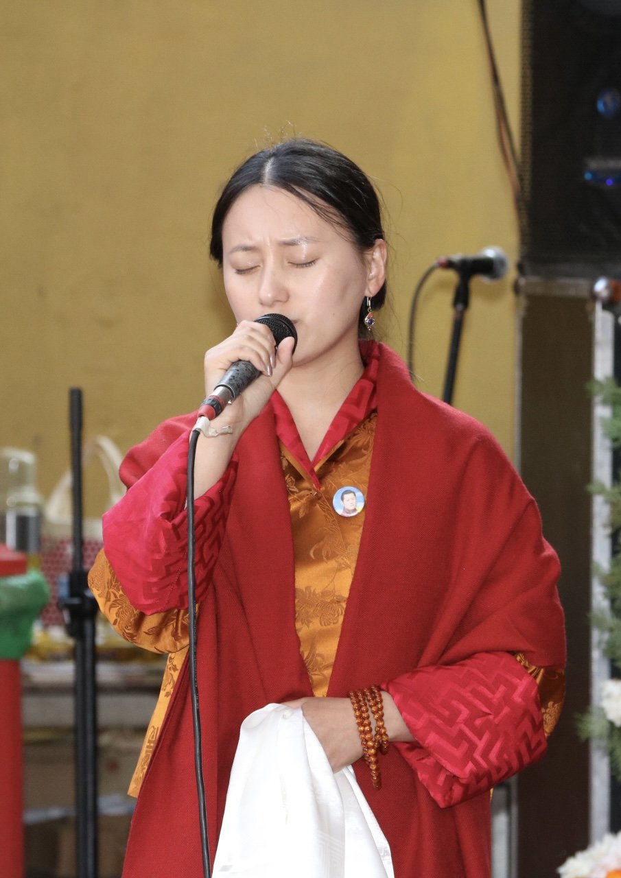 A woman wearing traditional Asian attire, holding a microphone with her eyes closed, appears to be singing.