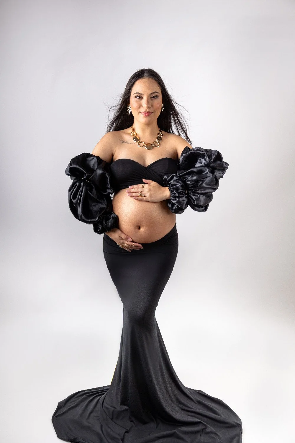 Femme enceinte portant une robe noire avec des manches bouffantes en satin, tenant son ventre