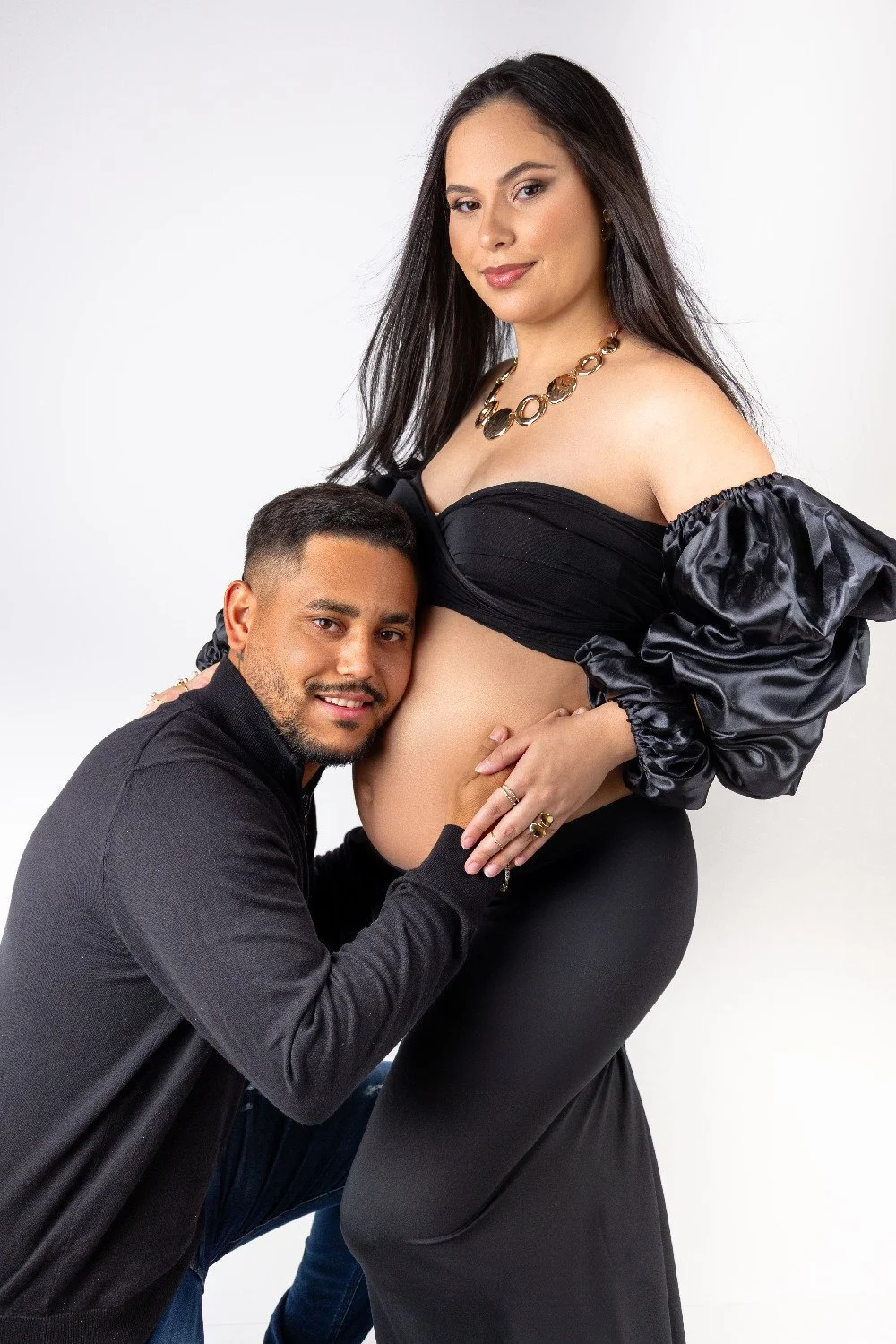 Un couple pose avec une femme enceinte dans un studio avec un fond blanc.