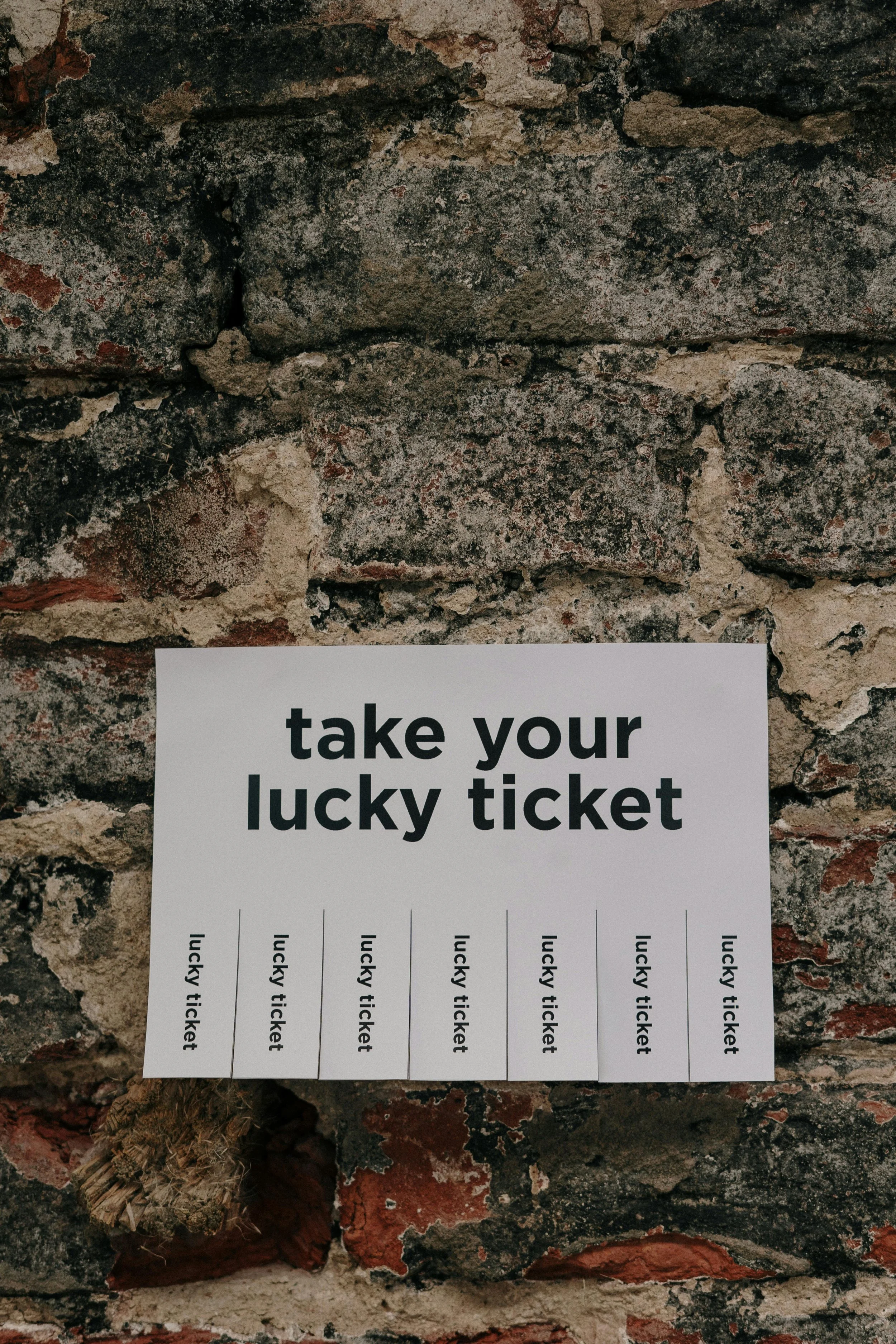 Een stuk papier met de tekst 'take your lucky ticket' en zeven genummerde uitsparingen voor tickets, vastgeplakt op een oude bakstenen muur.