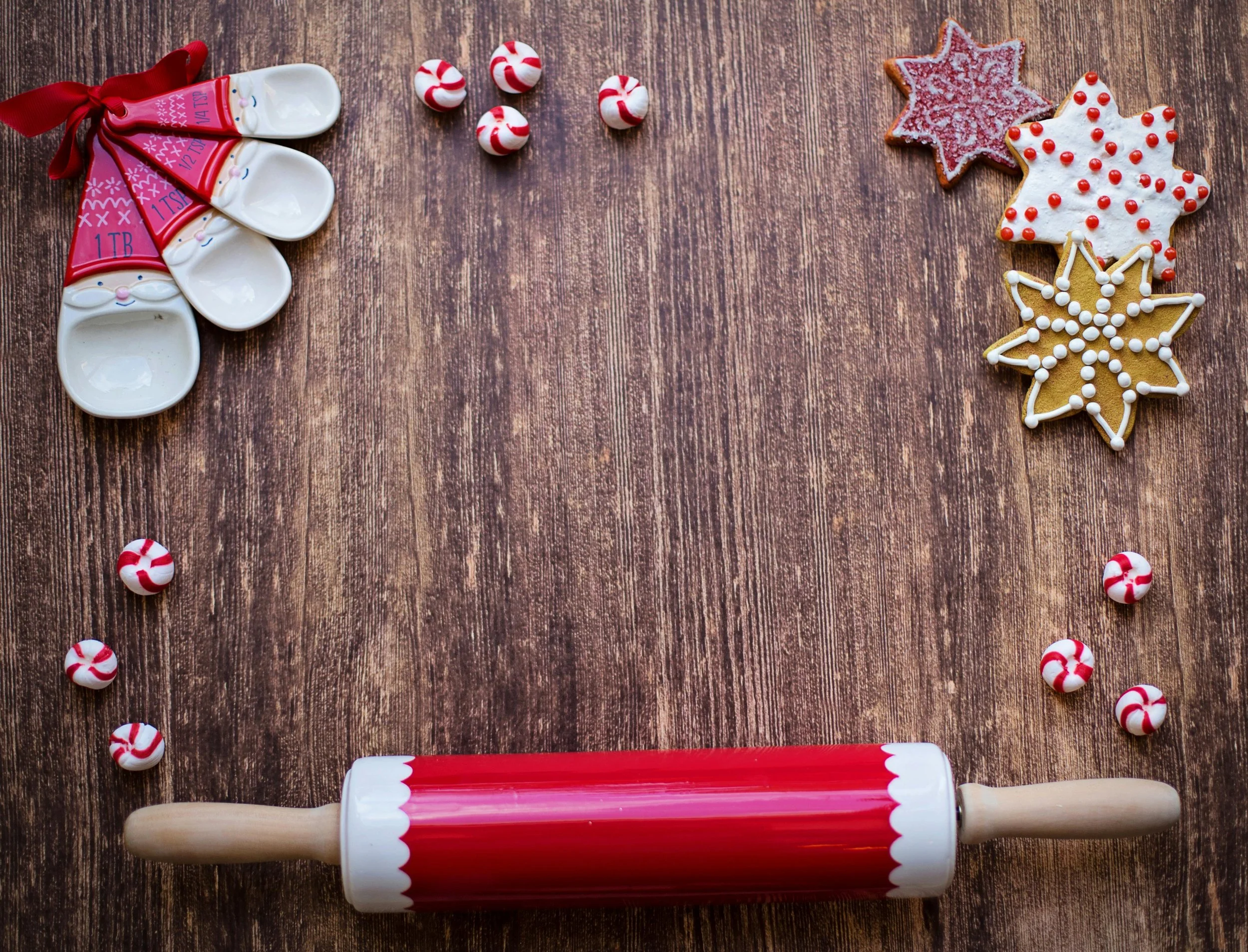 Decoratieve kerstkoekjes met suikerstrepen en stippen gelegen op een houten tafel, naast een rood en wit deegroller en kerstthema vorken en snoepjes.
