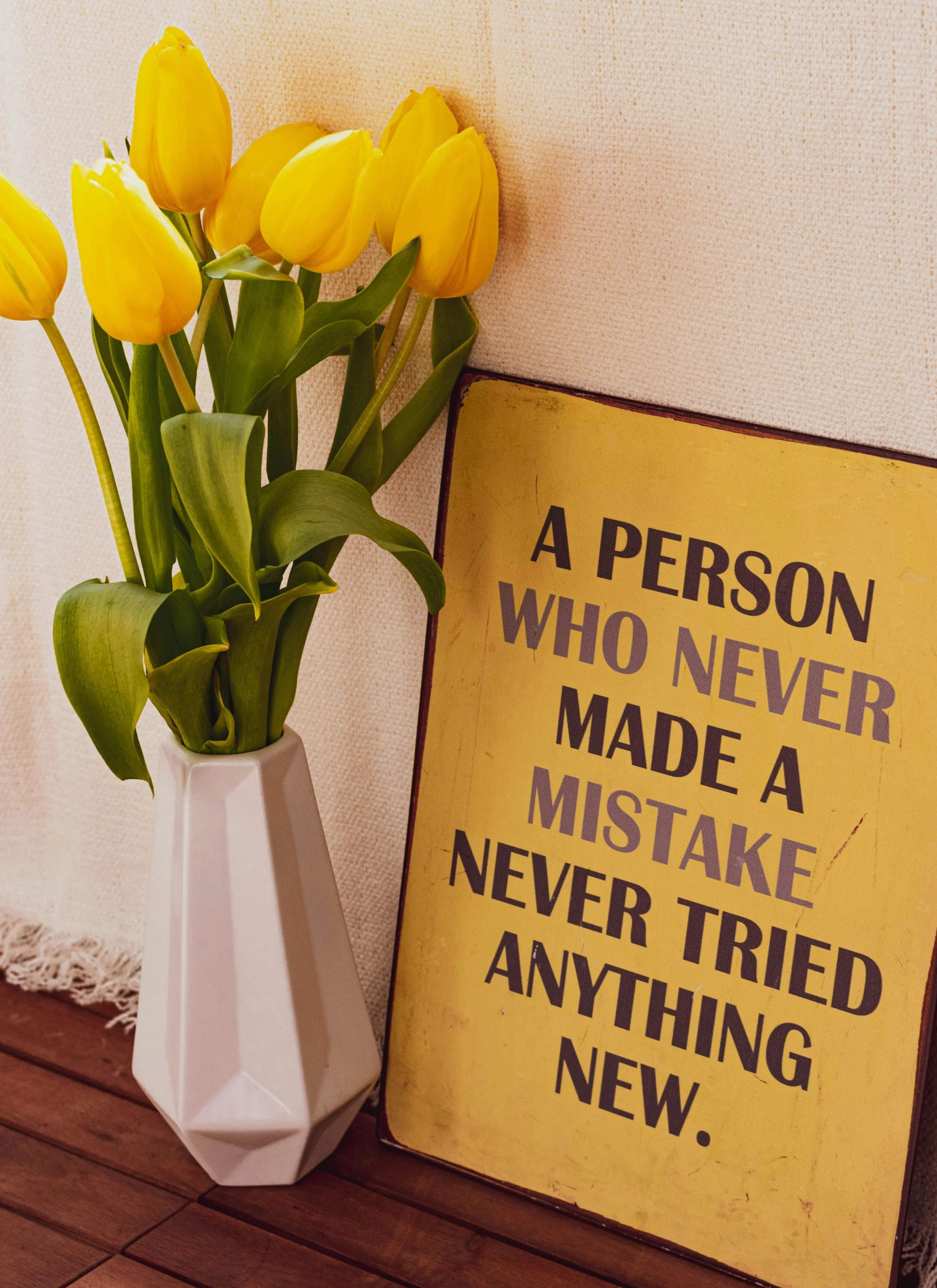 Verrijdbare gele tulpen in een witte vaas naast een geel poster met tekst.