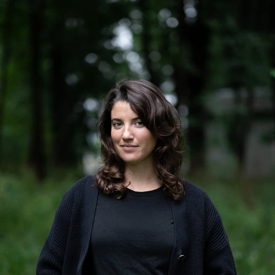 Woman in black cardigan standing in a forest setting