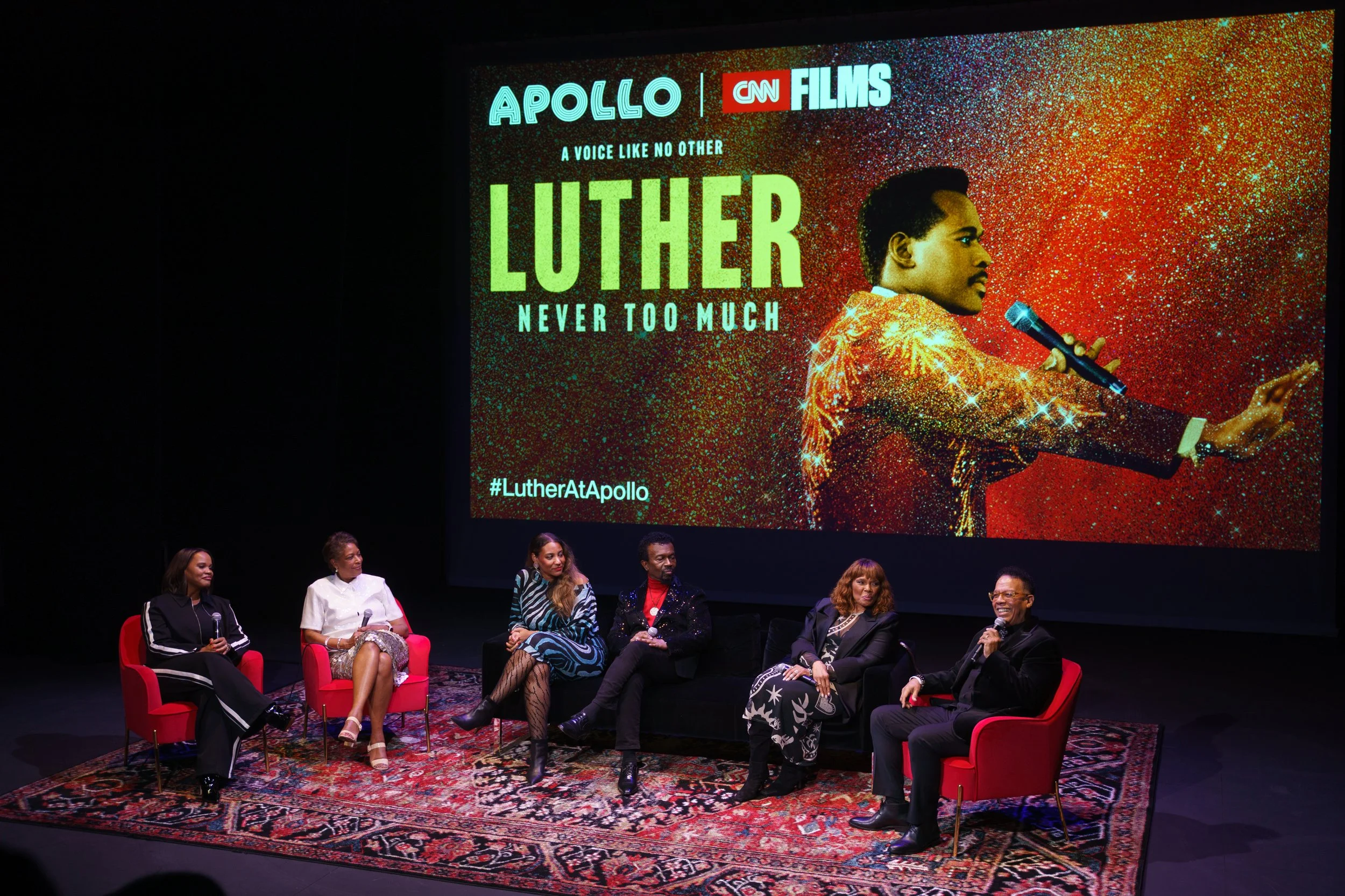  People sitting on stage beneath a screen 