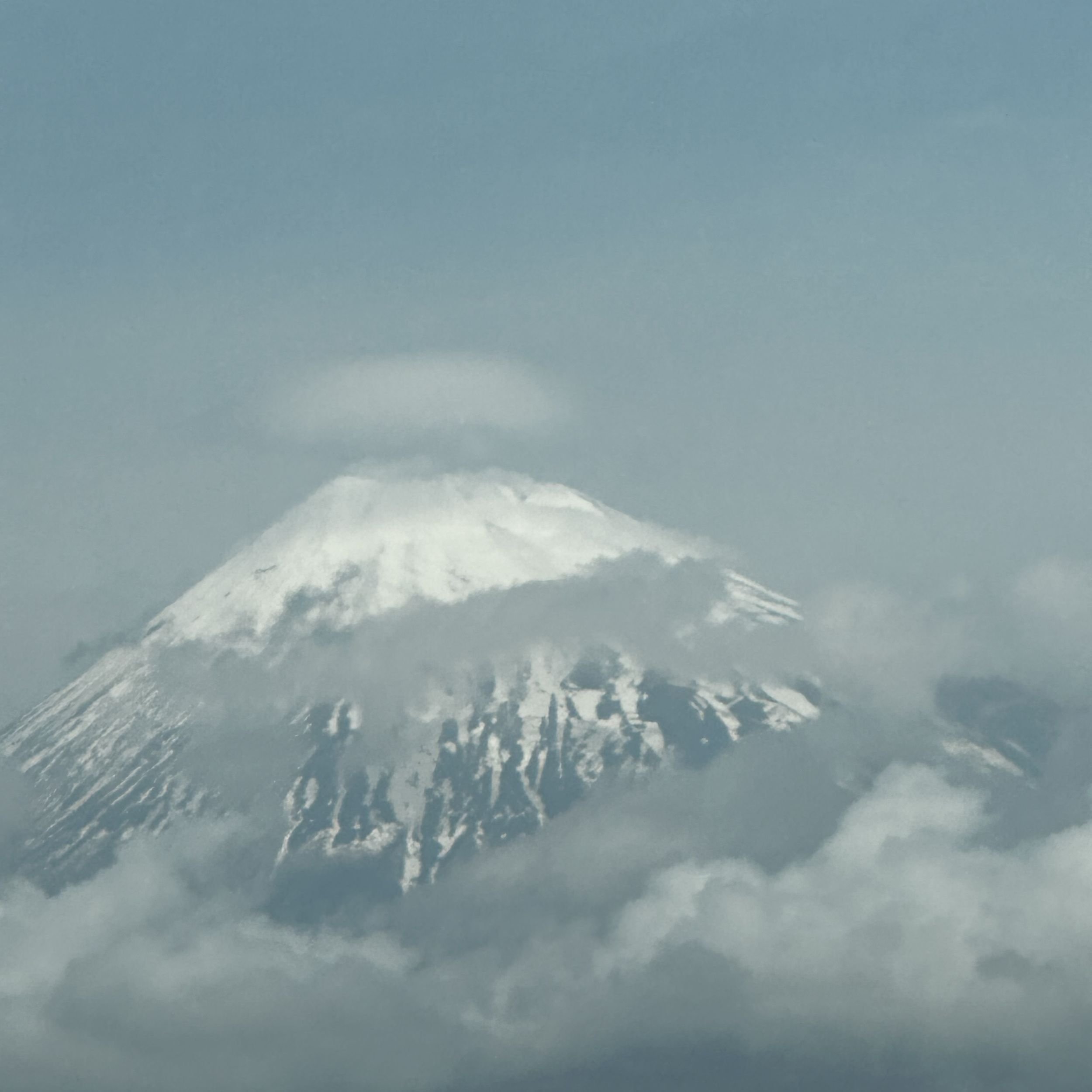 Mount Fuji viewed from the Shinkansen, with snow on the summit and low cloud across the lower slopes.