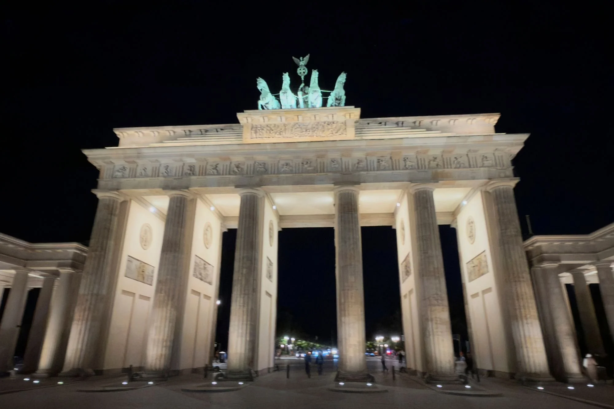 Low-angle view looking up at the illuminated Doric columns and copper Quadriga of the Brandenburg Gate on Pariser Platz at night.