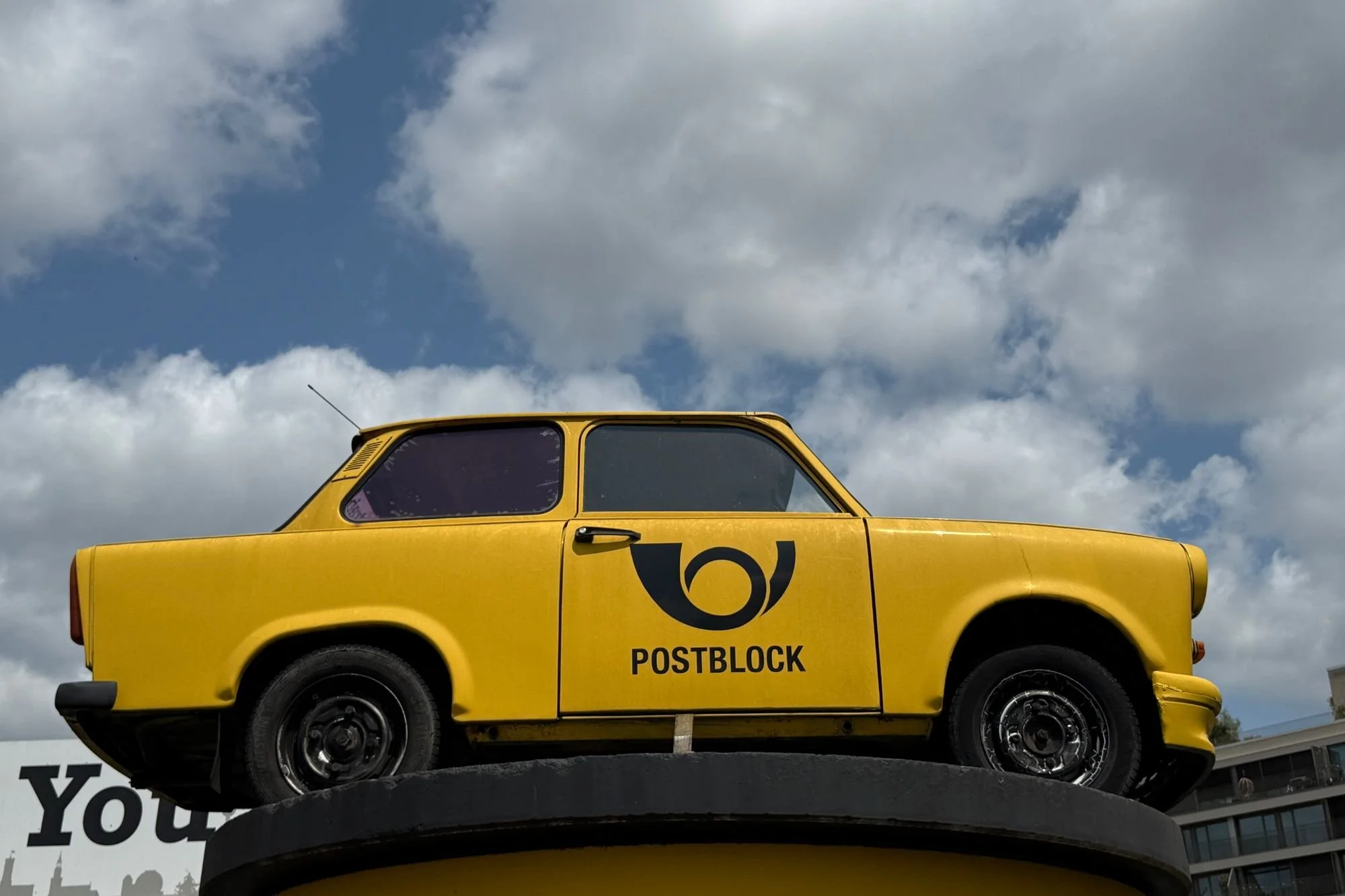 A trabant painted in Yellow Deutsche Post colours sits high above the ground at the Berlin Trabi Safari