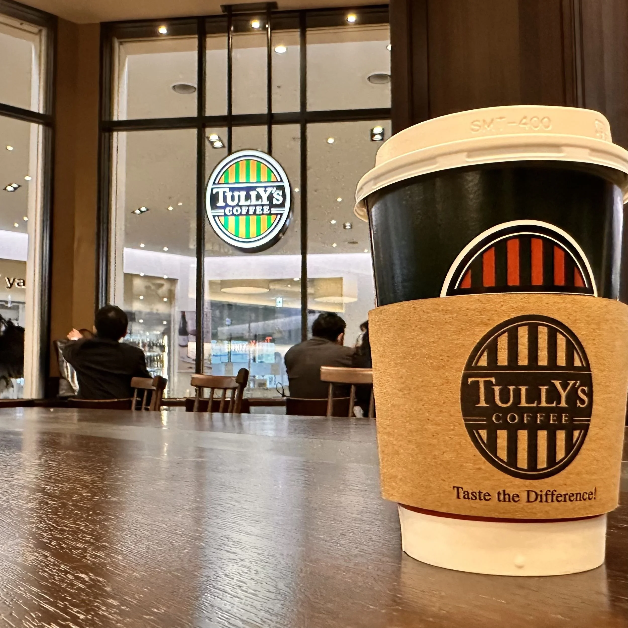 Tully’s Coffee takeaway cup on a wooden table inside a café at Shin-Osaka Station in Japan