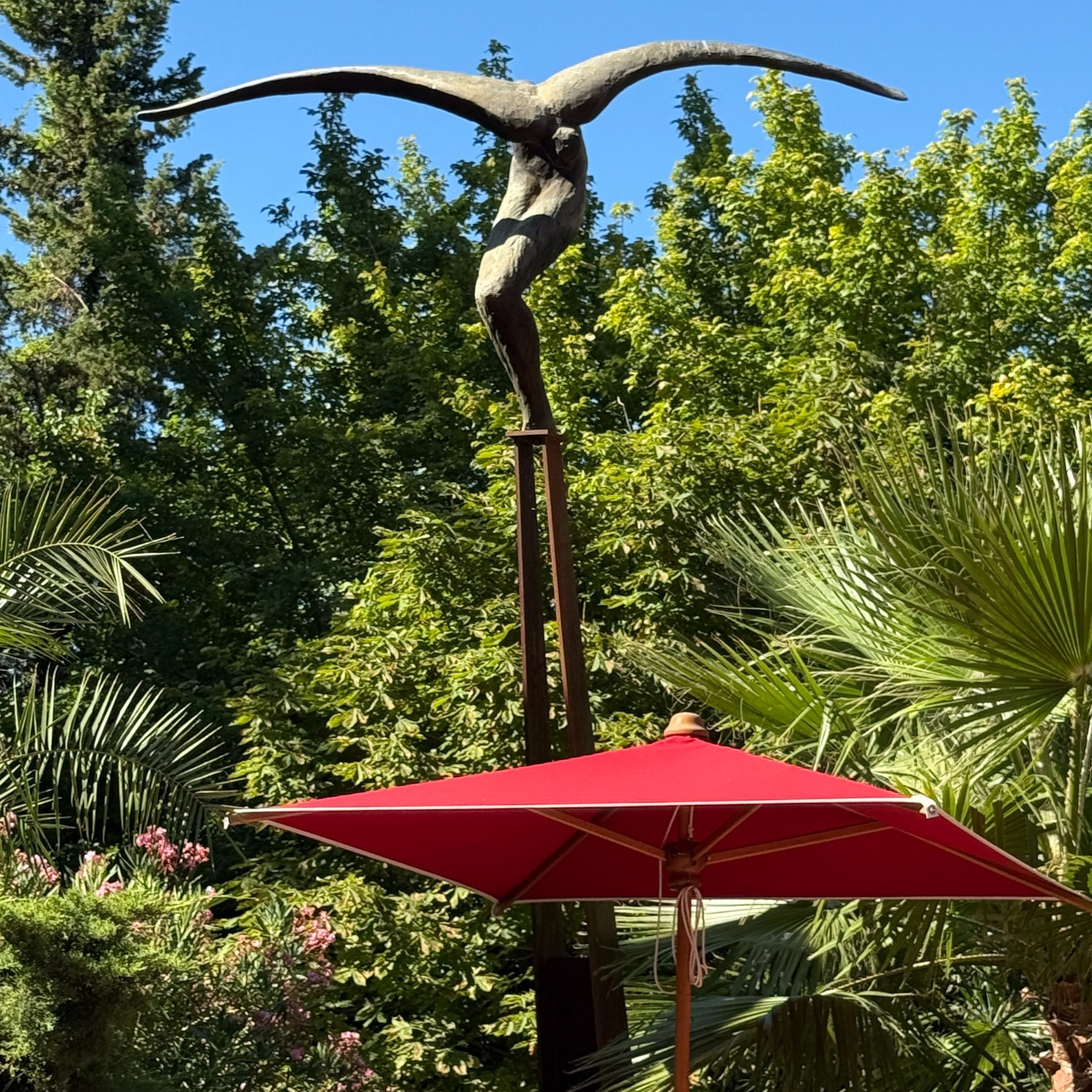 Winged sculpture above red parasol in the gardens of Villa Gallici
