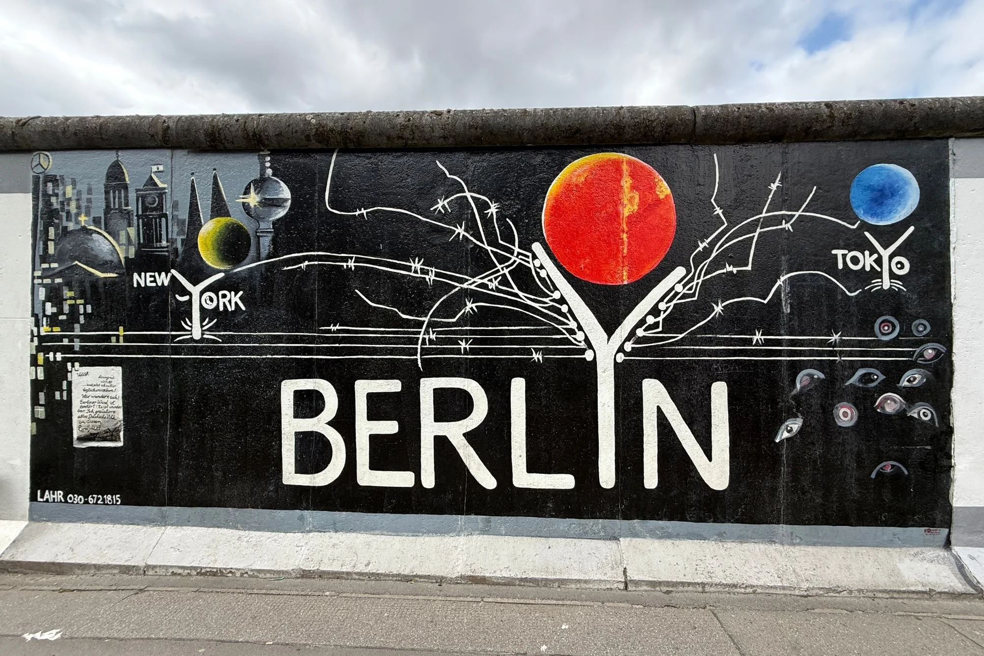 A vibrant mural painted on the Berlin Wall at the East Side Gallery, featuring the word "BERLIN" in bold white letters, a bright red sun, and a blue globe labeled "TOKYO"
