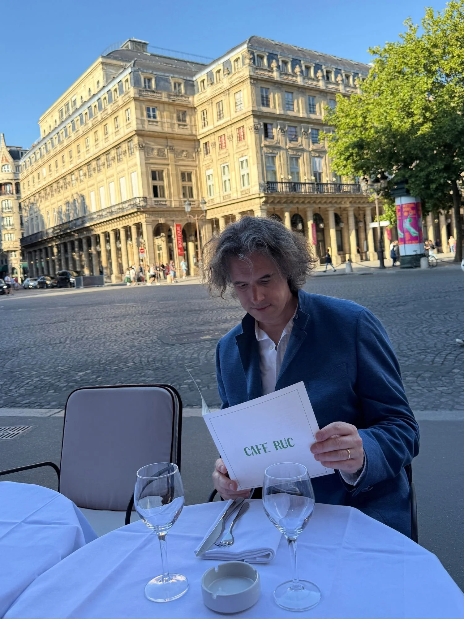 The author seated at an outdoor table reading the menu outside Café Ruc opposite the Comédie-Française in Paris.