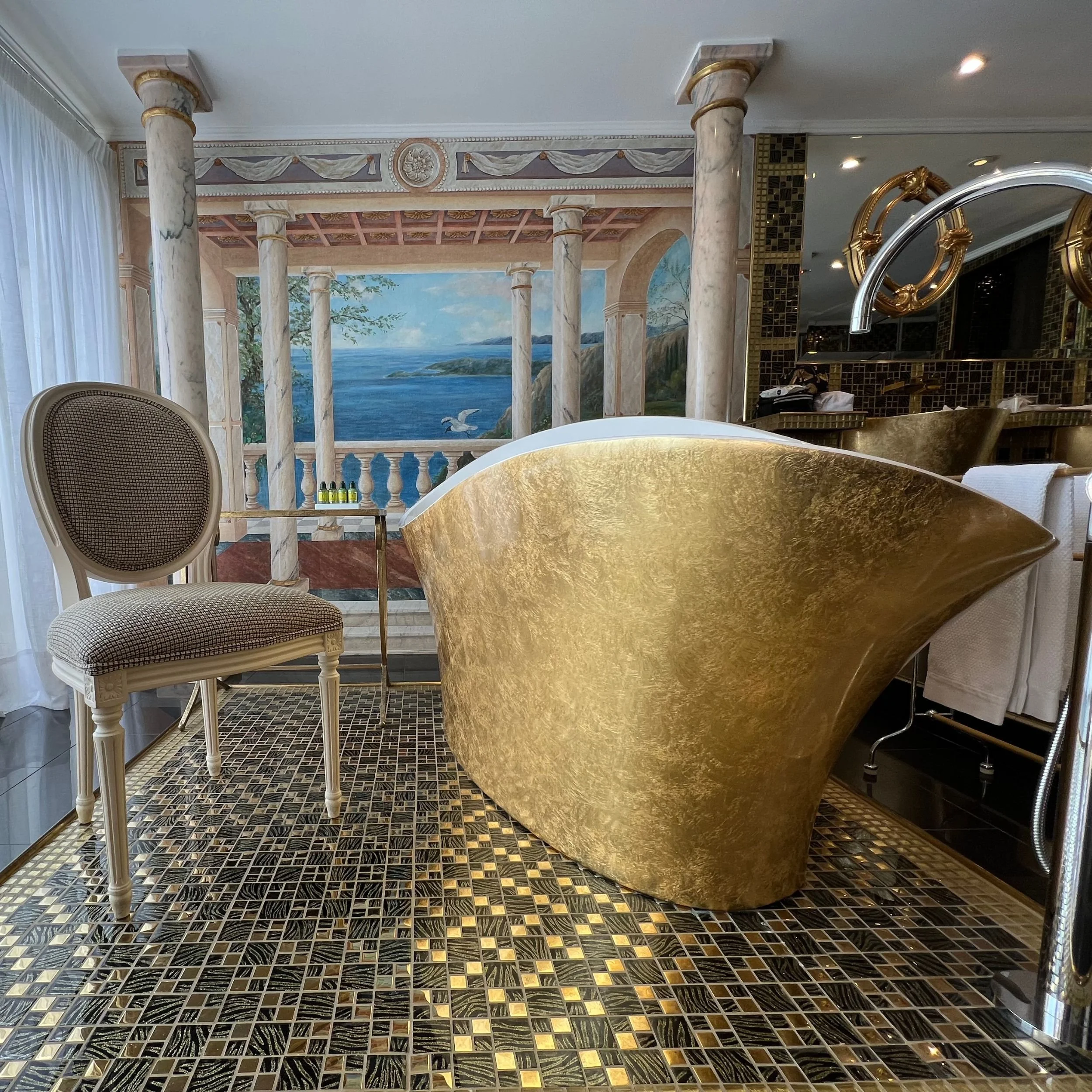 Gold freestanding bath with mural walls in the Panoramic Suite bathroom at Château de la Chèvre d’Or